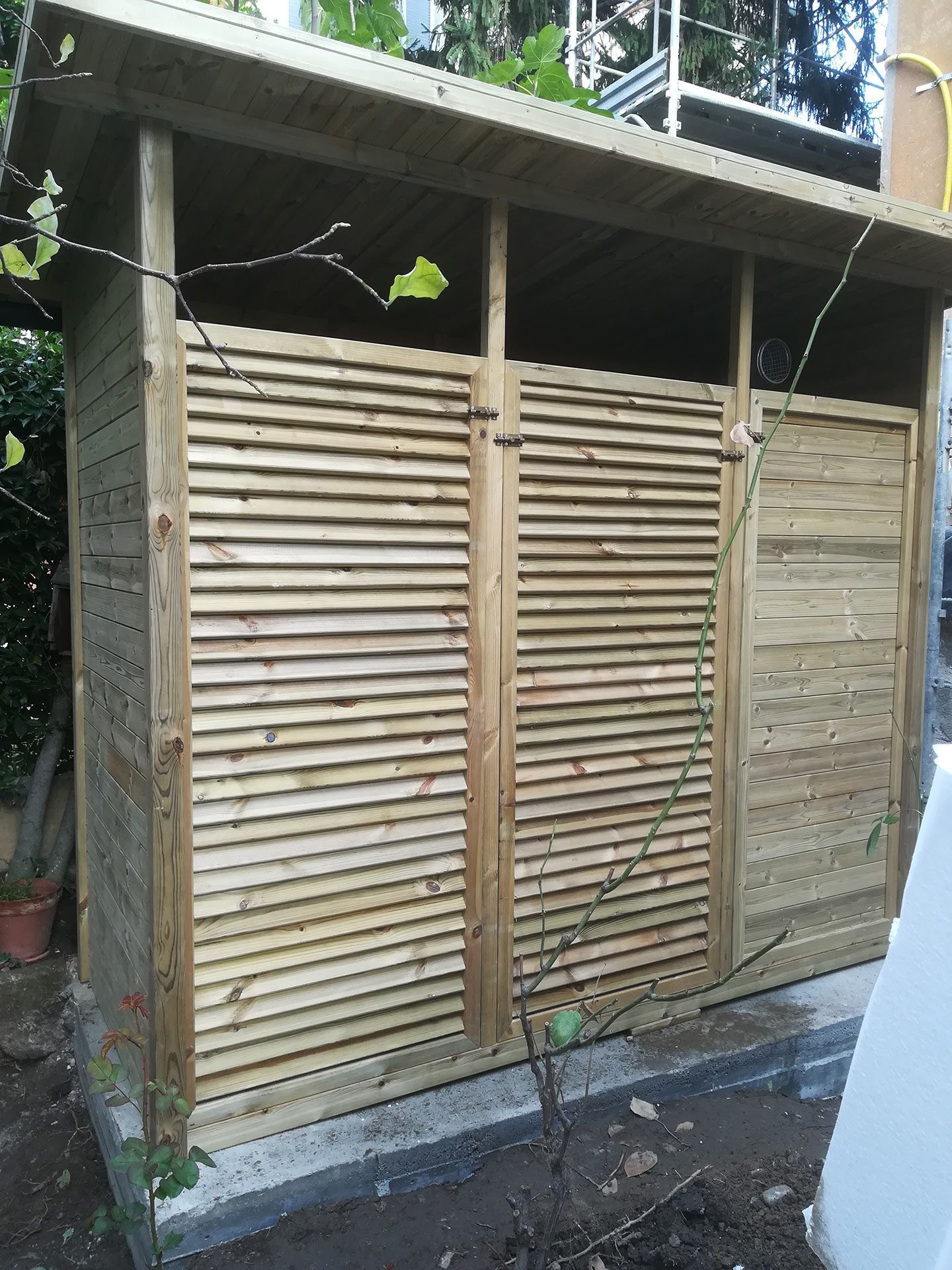 Casetta da giardino o recinzione in legno a doghe con una piccola porta, accanto a un vialetto e in una zona verde.