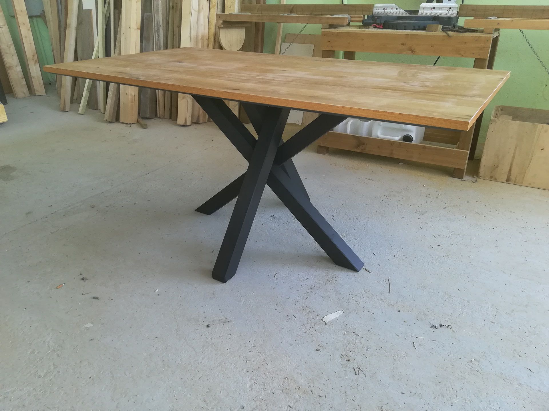 Tavolo in legno con gambe in metallo nero a forma di X in un ambiente da officina.