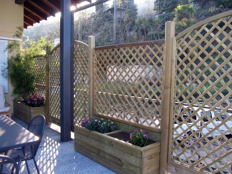 Patio con schermo frangivista a traliccio, fioriera, tavolo e sedie al sole