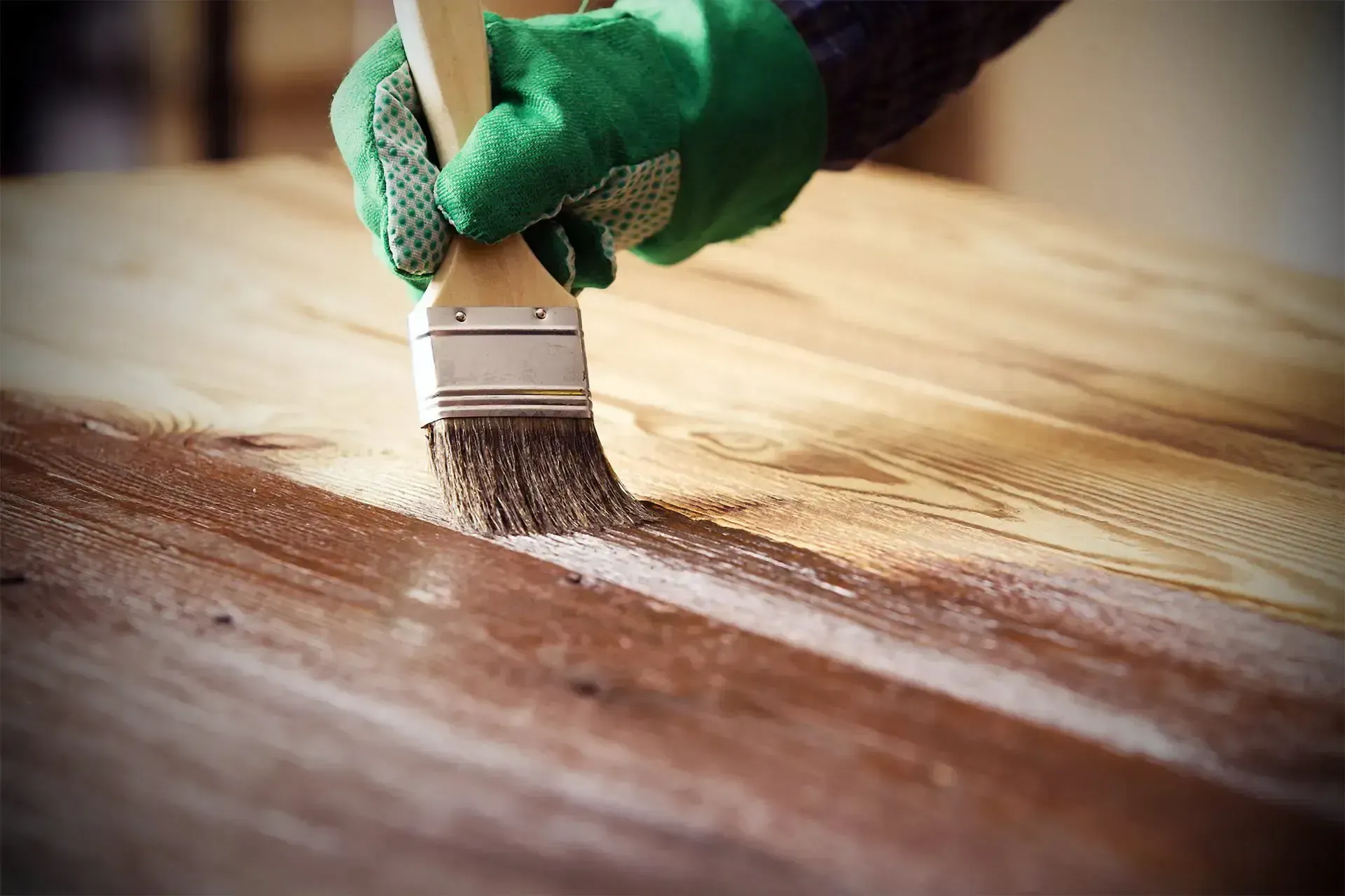 Mano guantata che applica la vernice su una superficie di legno con un pennello