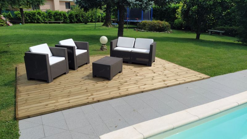 Set di mobili da giardino per esterni su una terrazza in legno, accanto a un prato e a un vialetto a bordo piscina.