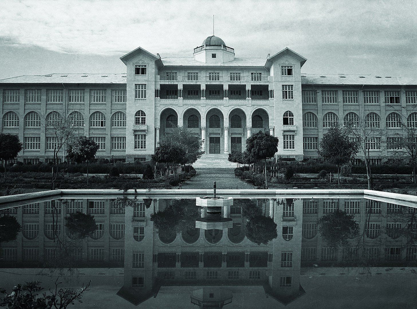 A black and white photo of a large building with a pond in front of it