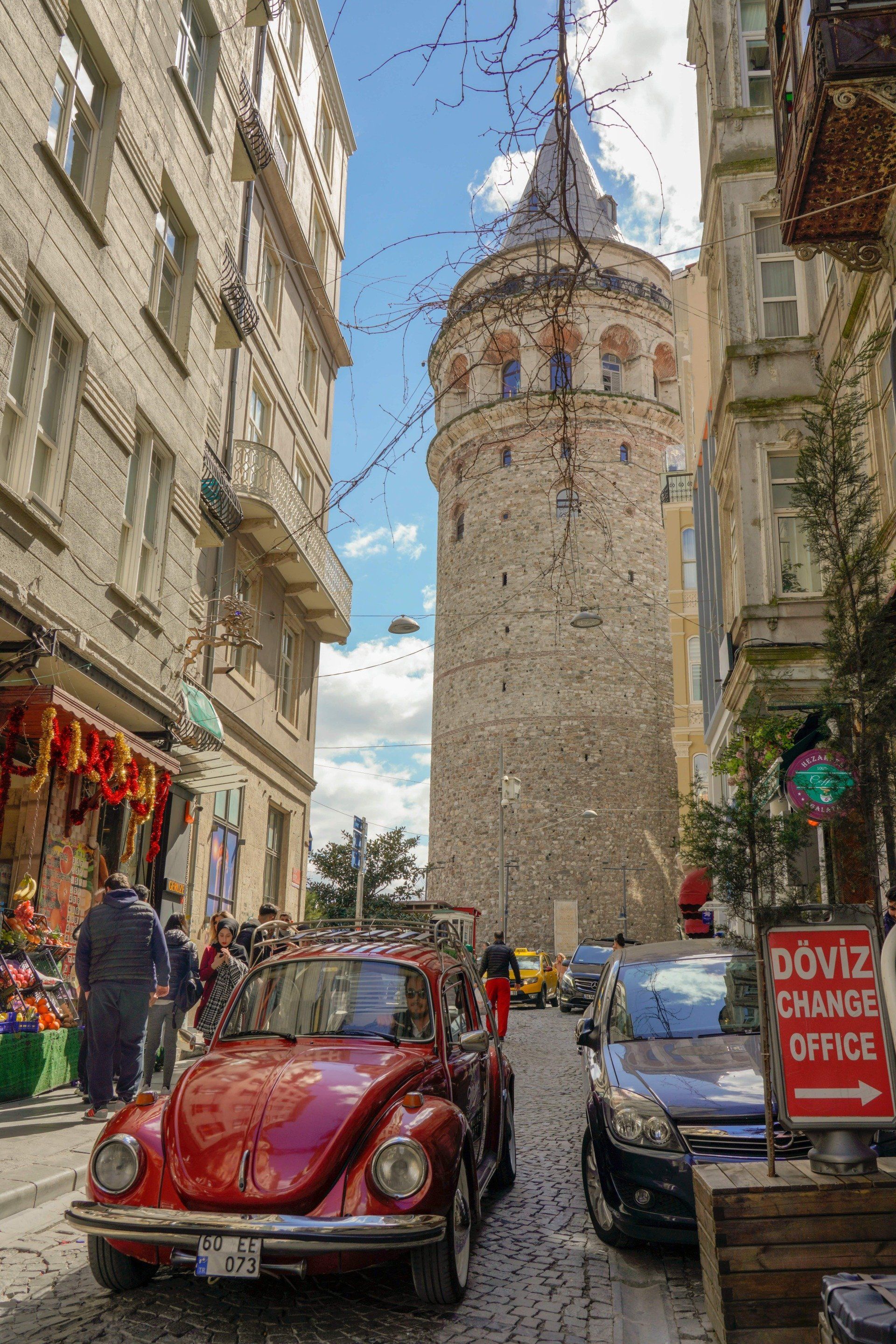A red beetle is parked in the middle of a narrow street.