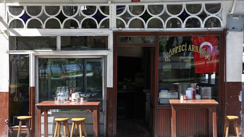 A restaurant with tables and stools in front of it.