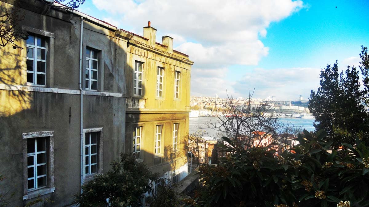 A large building with a lot of windows is sitting on top of a hill overlooking a body of water.