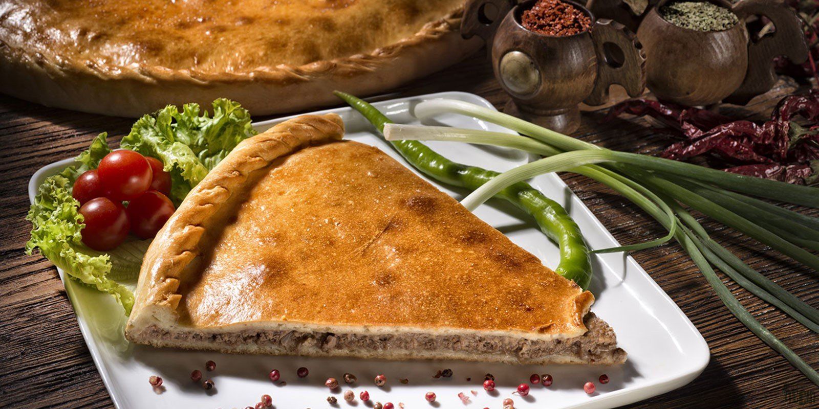 A slice of pie is on a white plate with green onions and tomatoes.