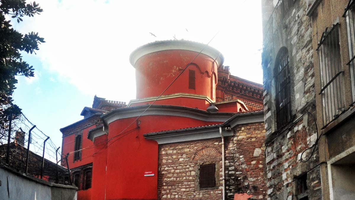 A red building with a circular roof is surrounded by brick buildings.