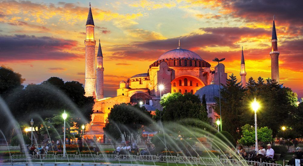 A mosque with a fountain in front of it at sunset.