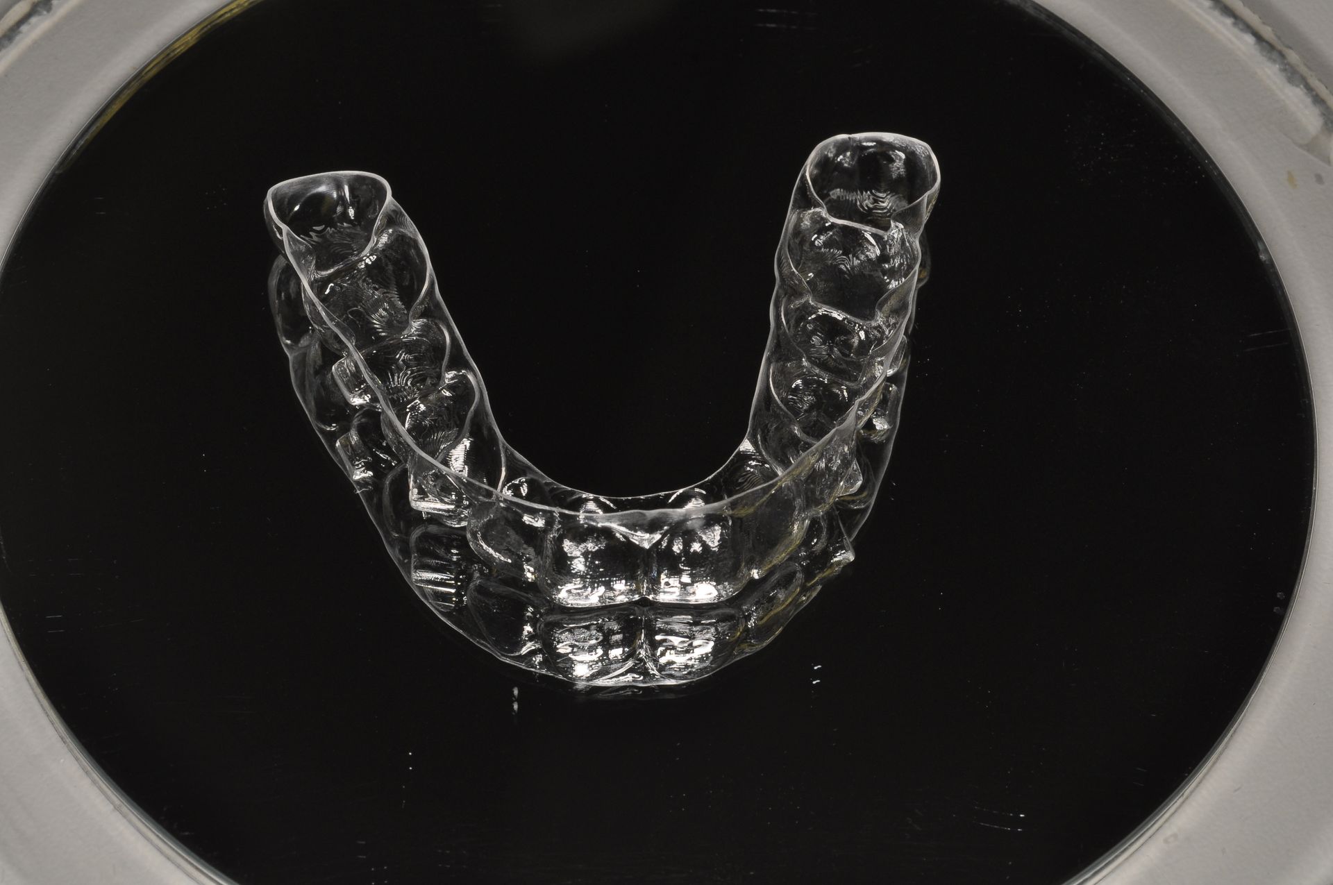 Allineatore dentale trasparente in una custodia rotonda nera su sfondo scuro.