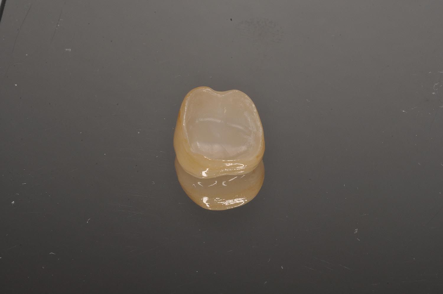 Piccolo oggetto traslucido color ambra a forma di dente su una superficie scura