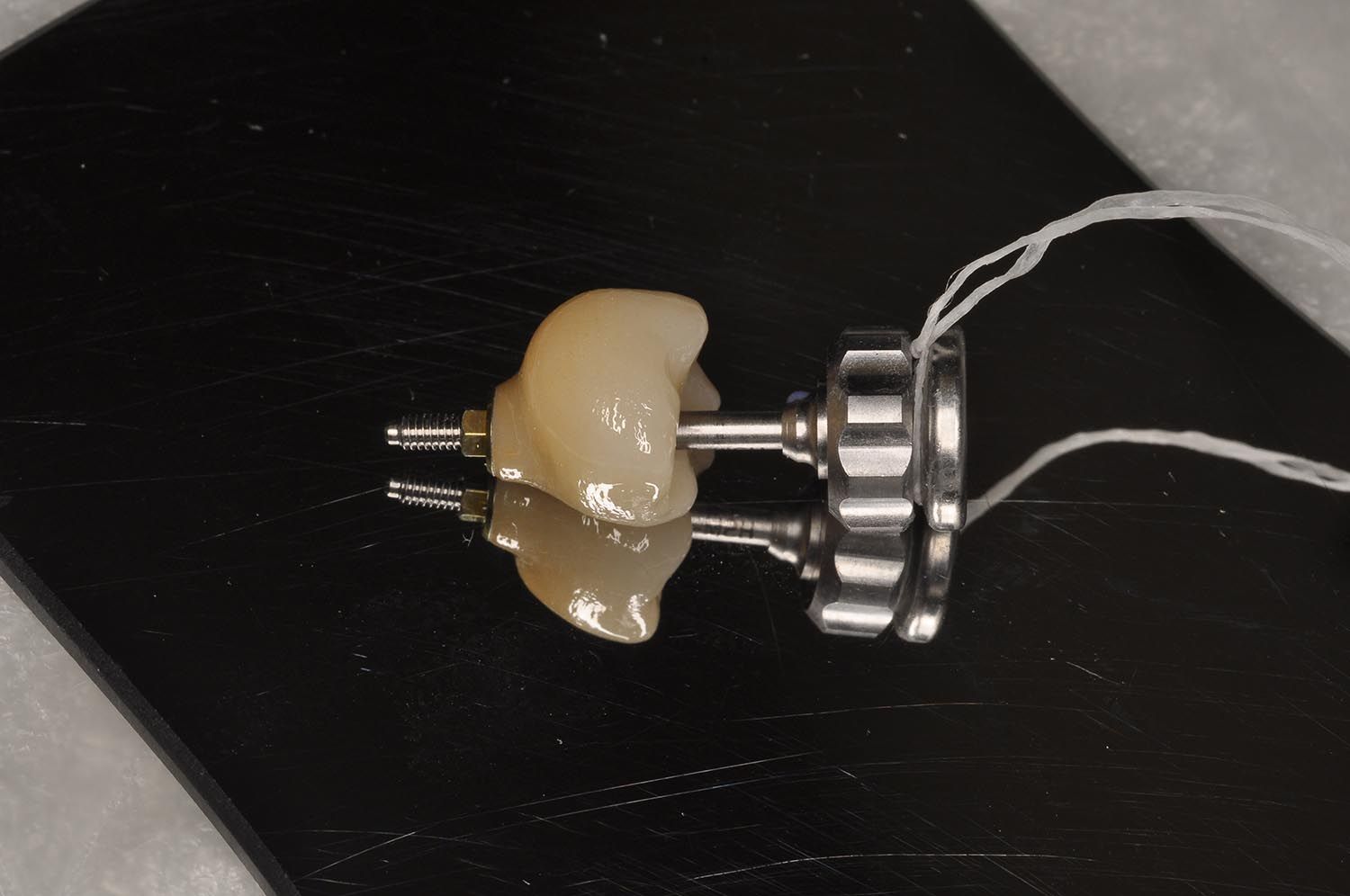 Dente protesico dentale fissato a un supporto metallico su una superficie nera
