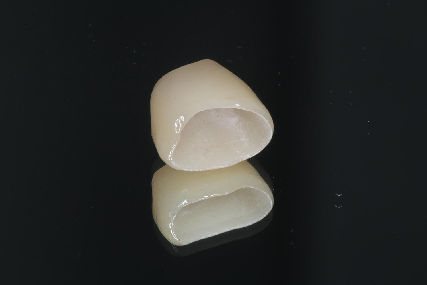 Due corone dentali color bianco sporco su sfondo nero, una sovrapposta all'altra.