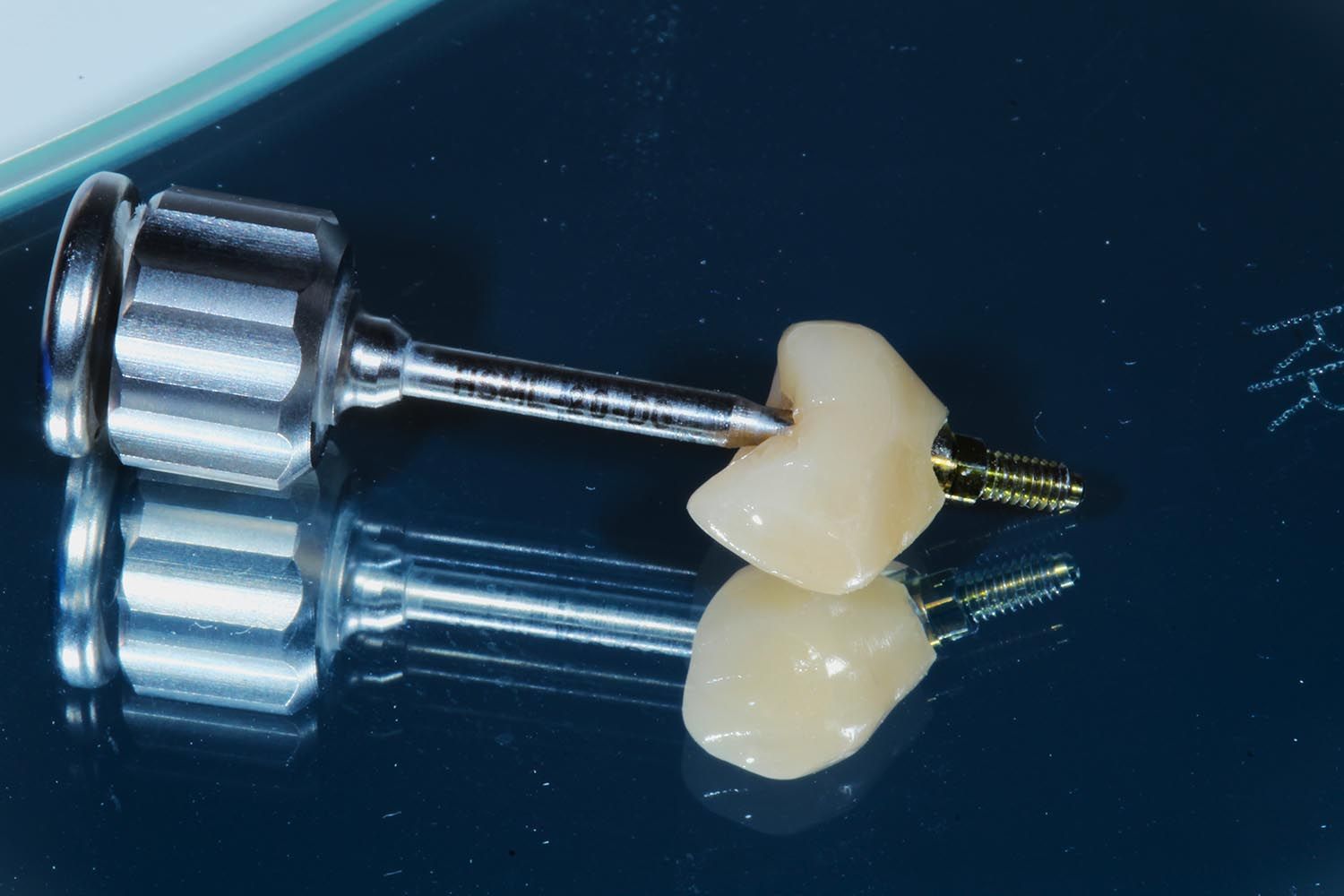 Due strumenti odontoiatrici metallici accanto a due otturazioni a forma di dente su una superficie scura e riflettente