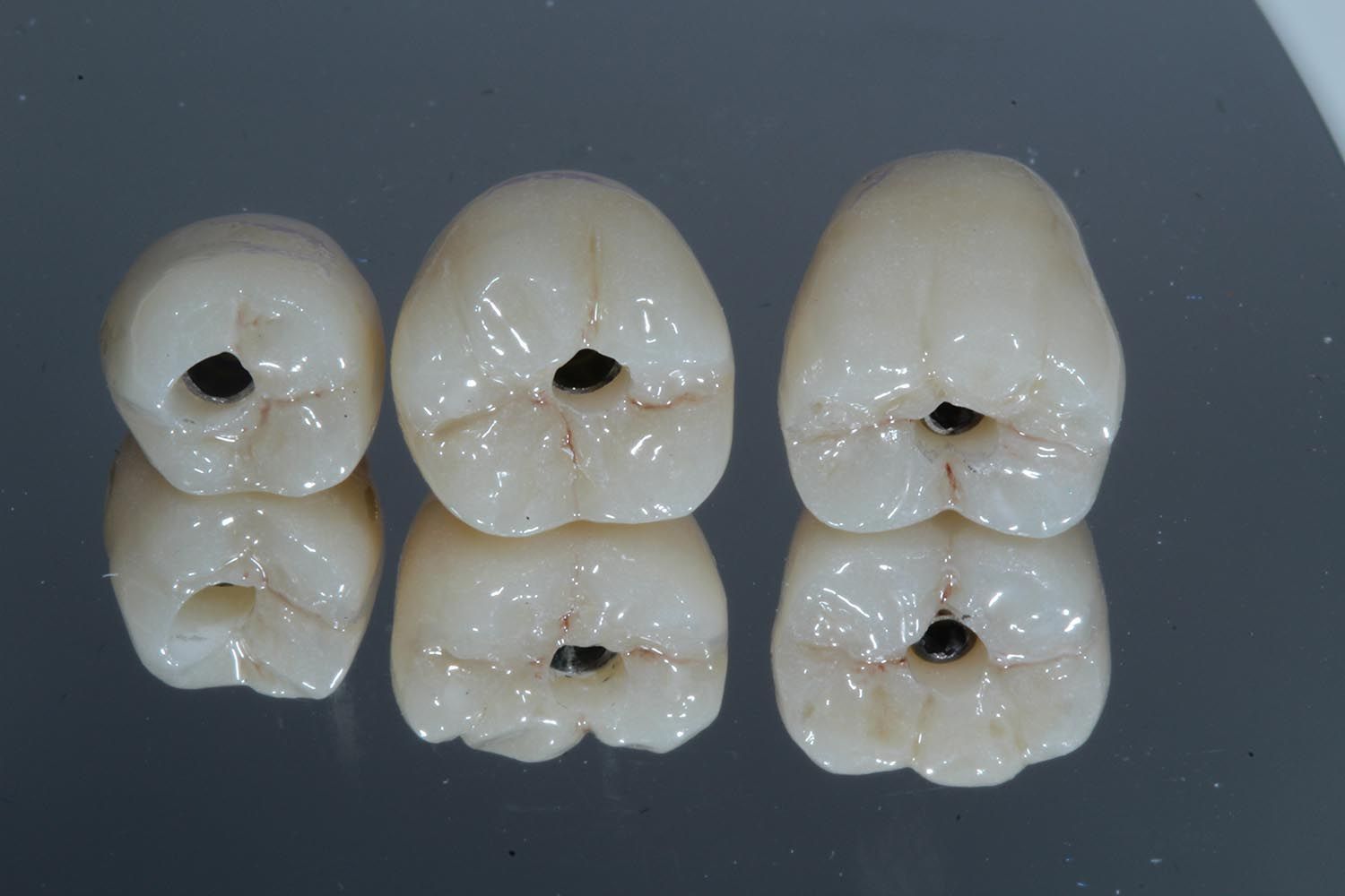 Sei corone dentali bianche con fori centrali neri disposte su una superficie grigia