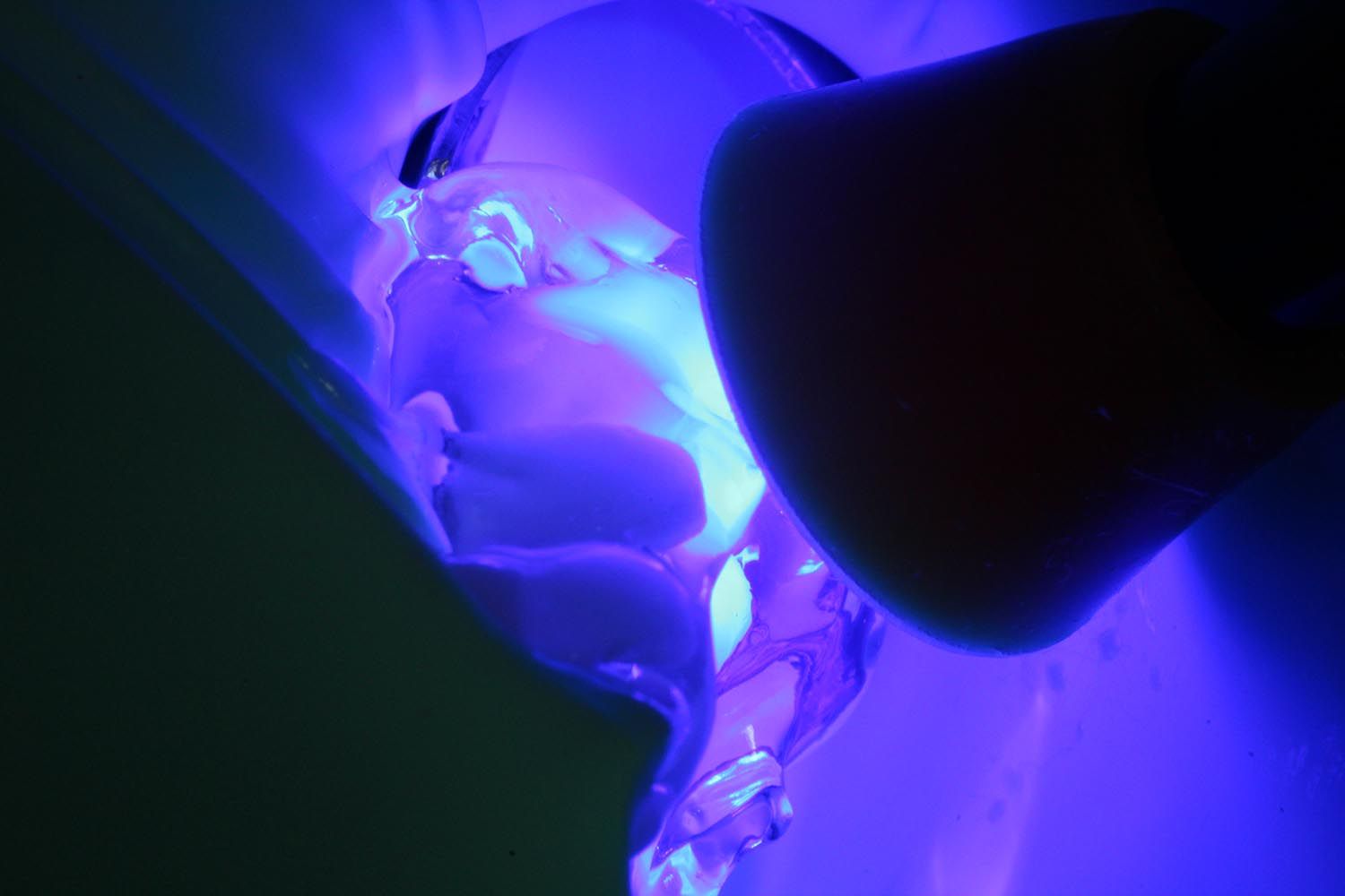 Un liquido blu fosforescente viene versato in un contenitore trasparente, primo piano in penombra.