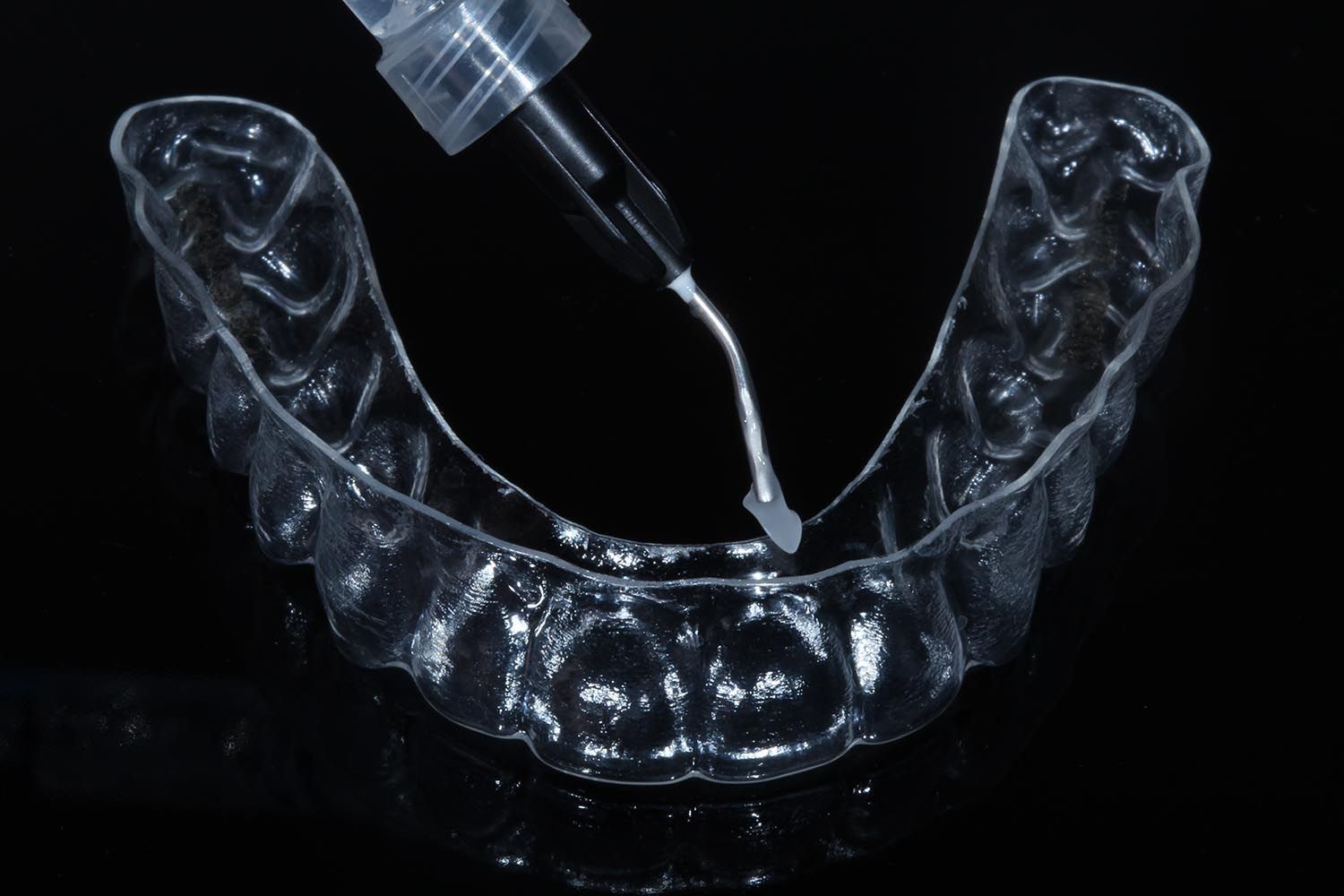 Allineatore dentale trasparente con contagocce per l'applicazione di liquido su sfondo nero.