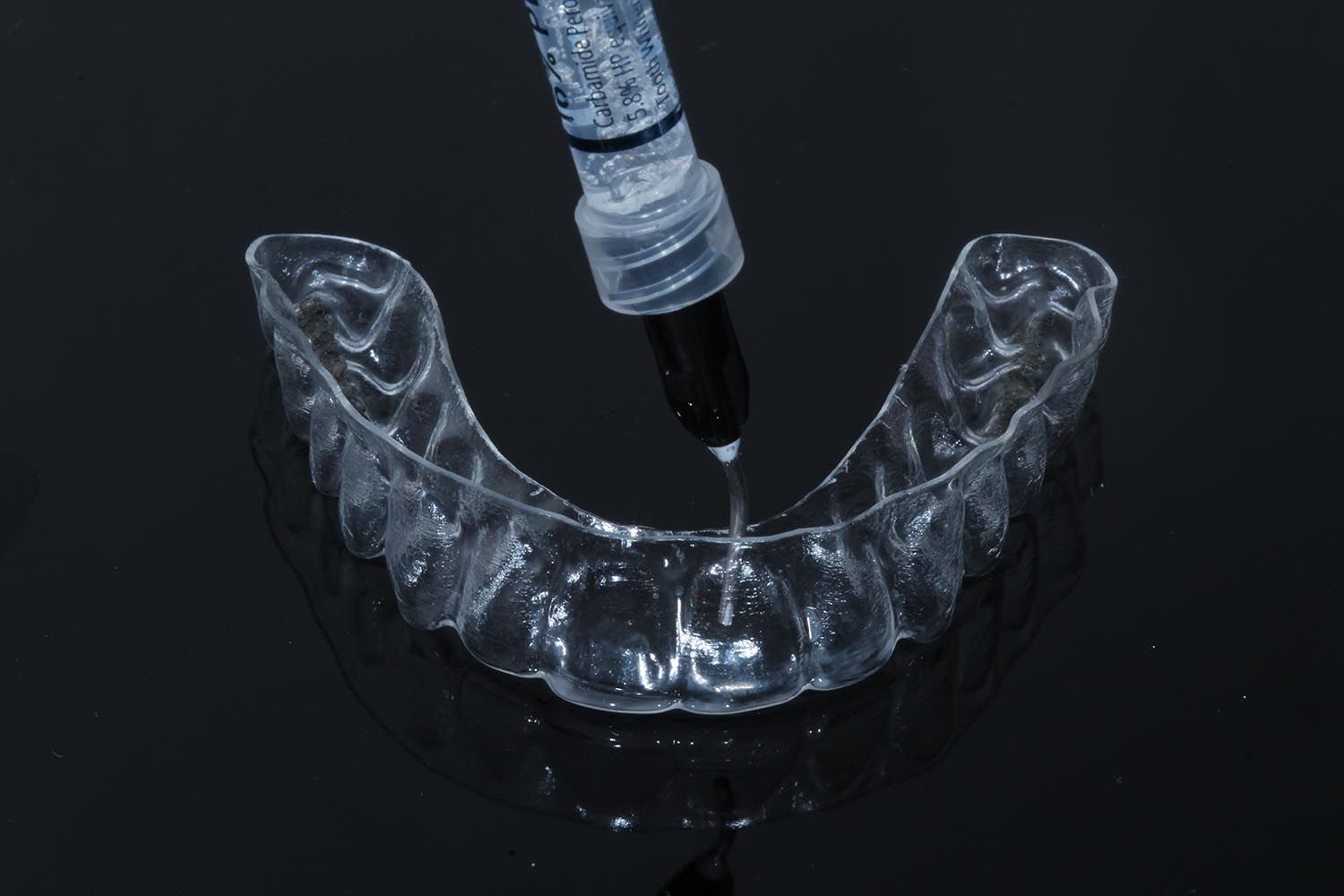 Un allineatore dentale trasparente viene riempito con un liquido nero tramite un contagocce su una superficie scura.
