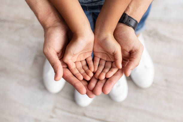 Adult's hands cupping child's hands, close-up. White shoes and denim visible.
