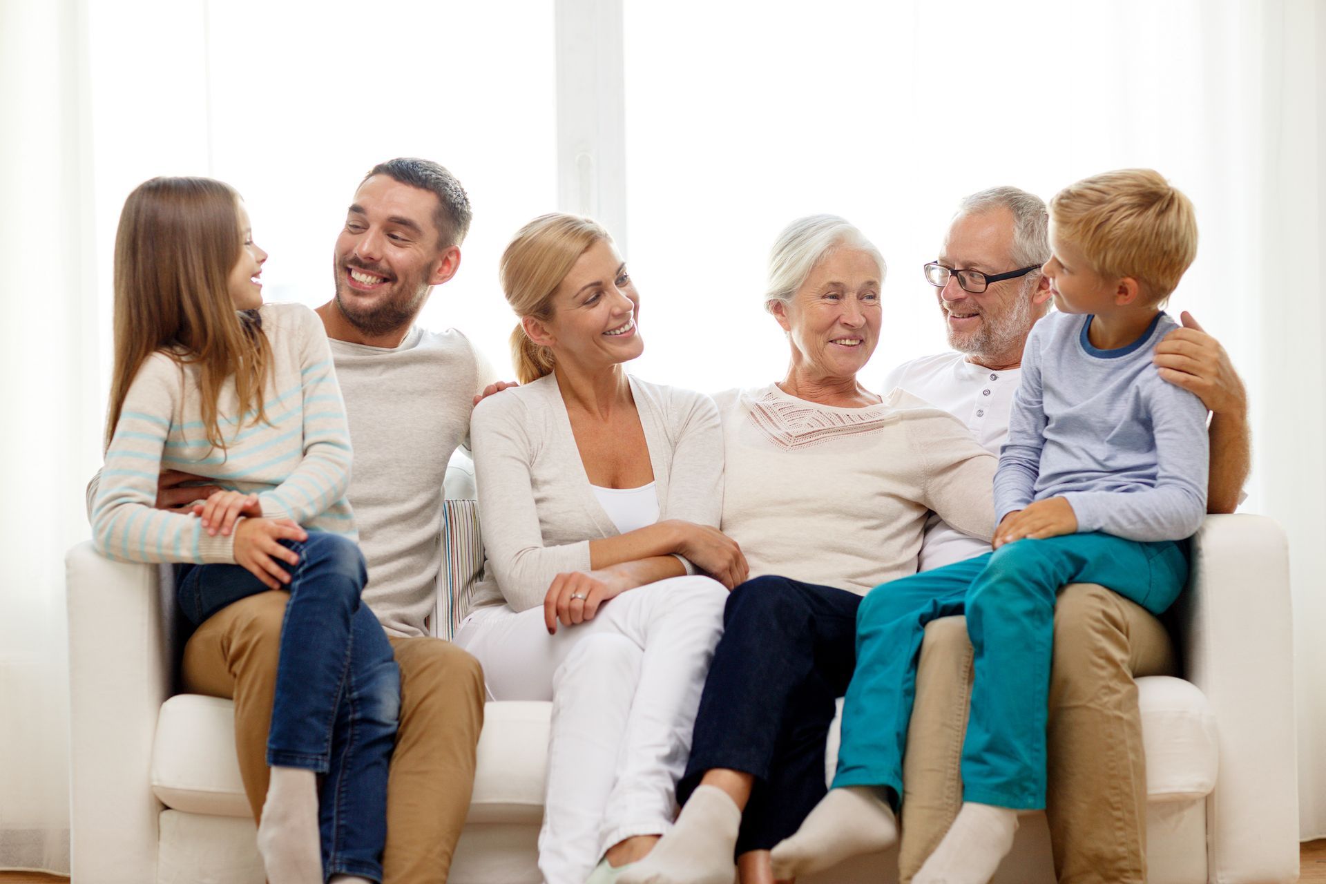 Multi-generational family smiling together on a white couch in a well-lit room.
