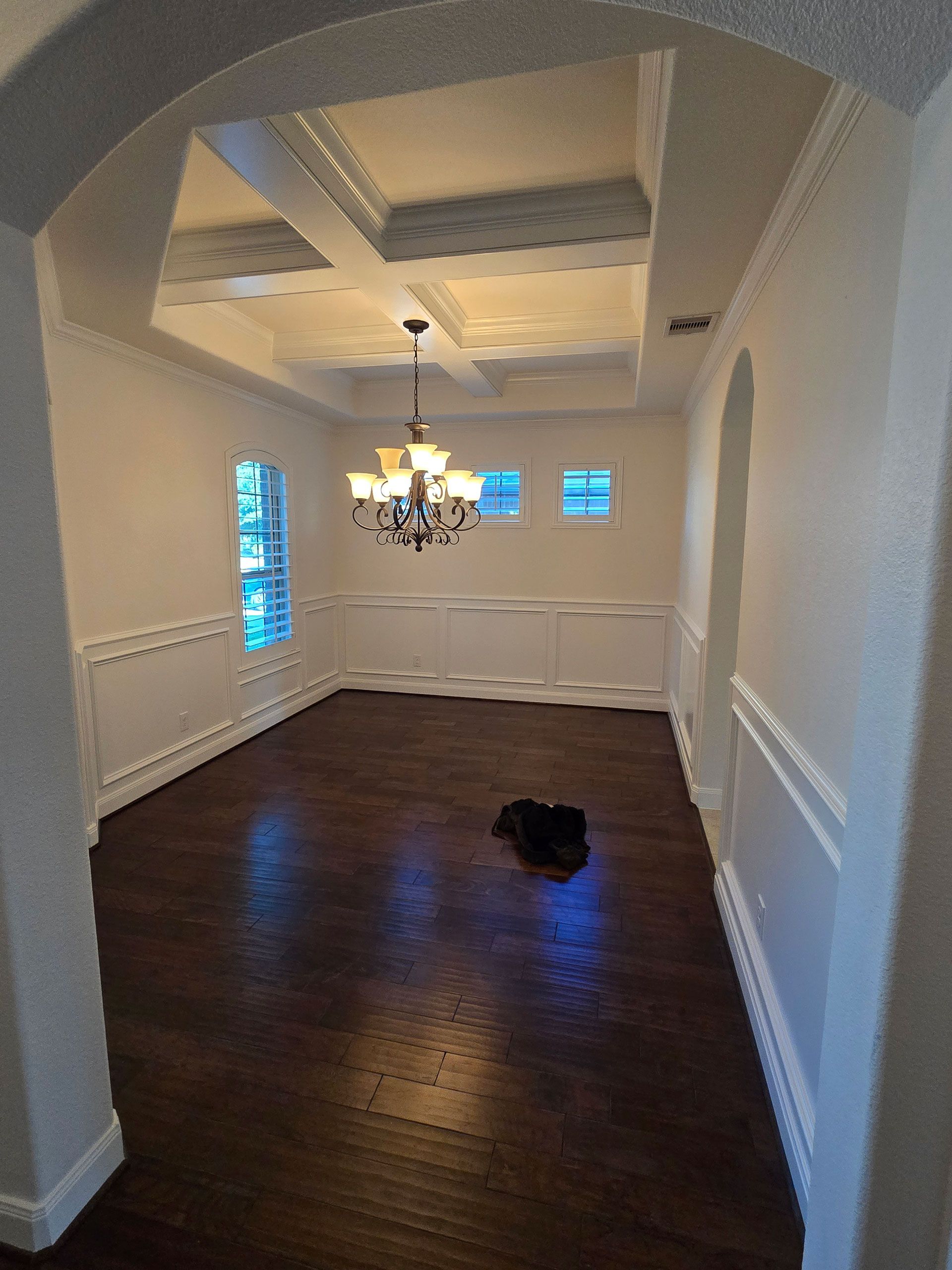 Formal dining room with dark wood floor, white walls and ceiling, chandelier.
