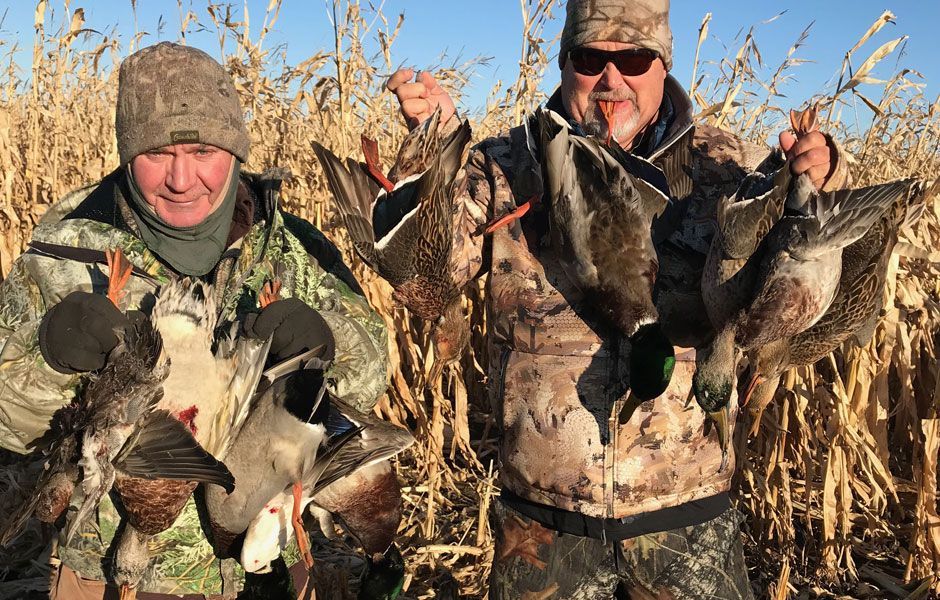 Two men are standing in a field holding ducks.
