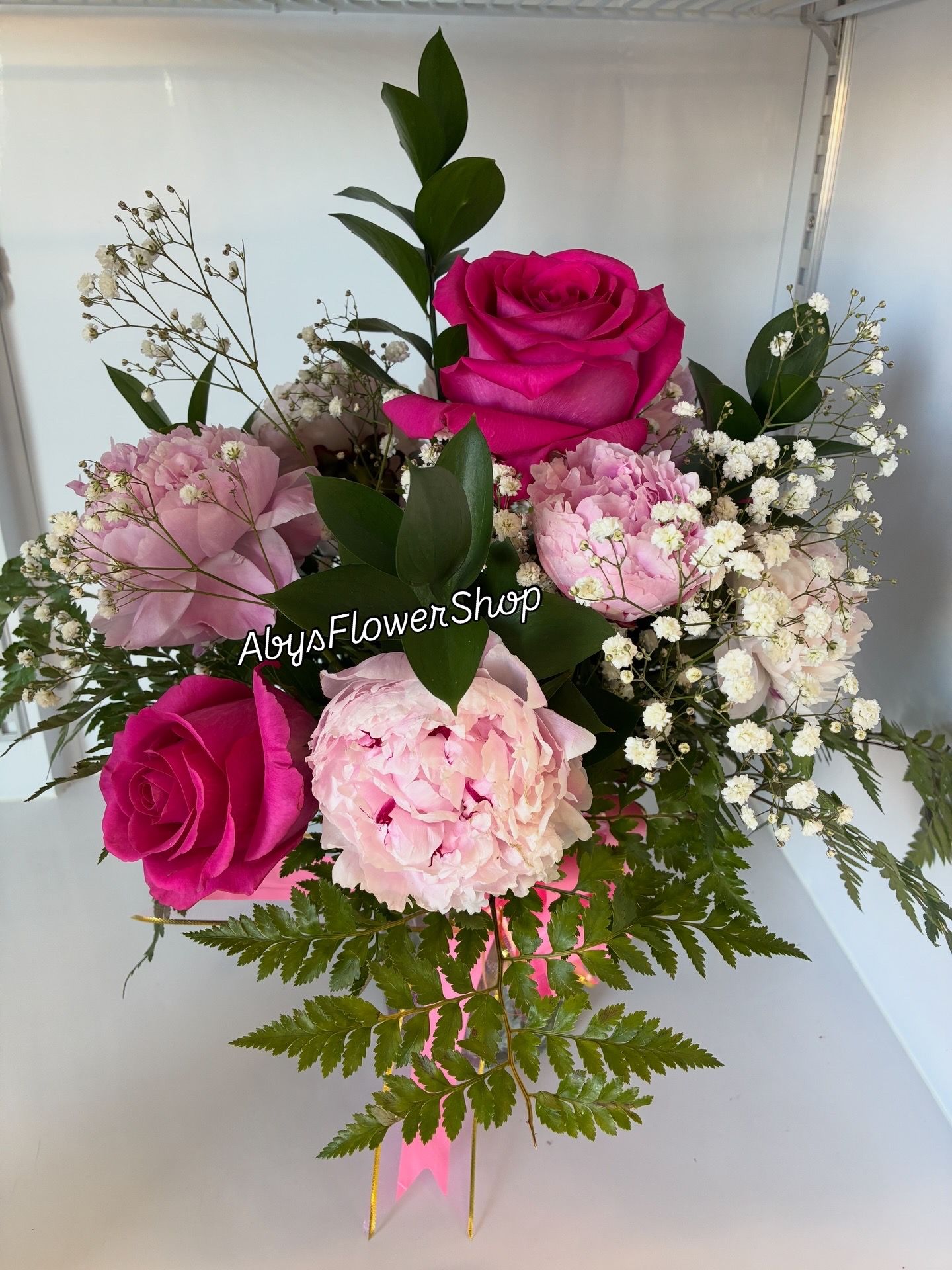 A bouquet of pink roses, light pink hydrangeas, baby's breath, and green foliage against a plain white background.
