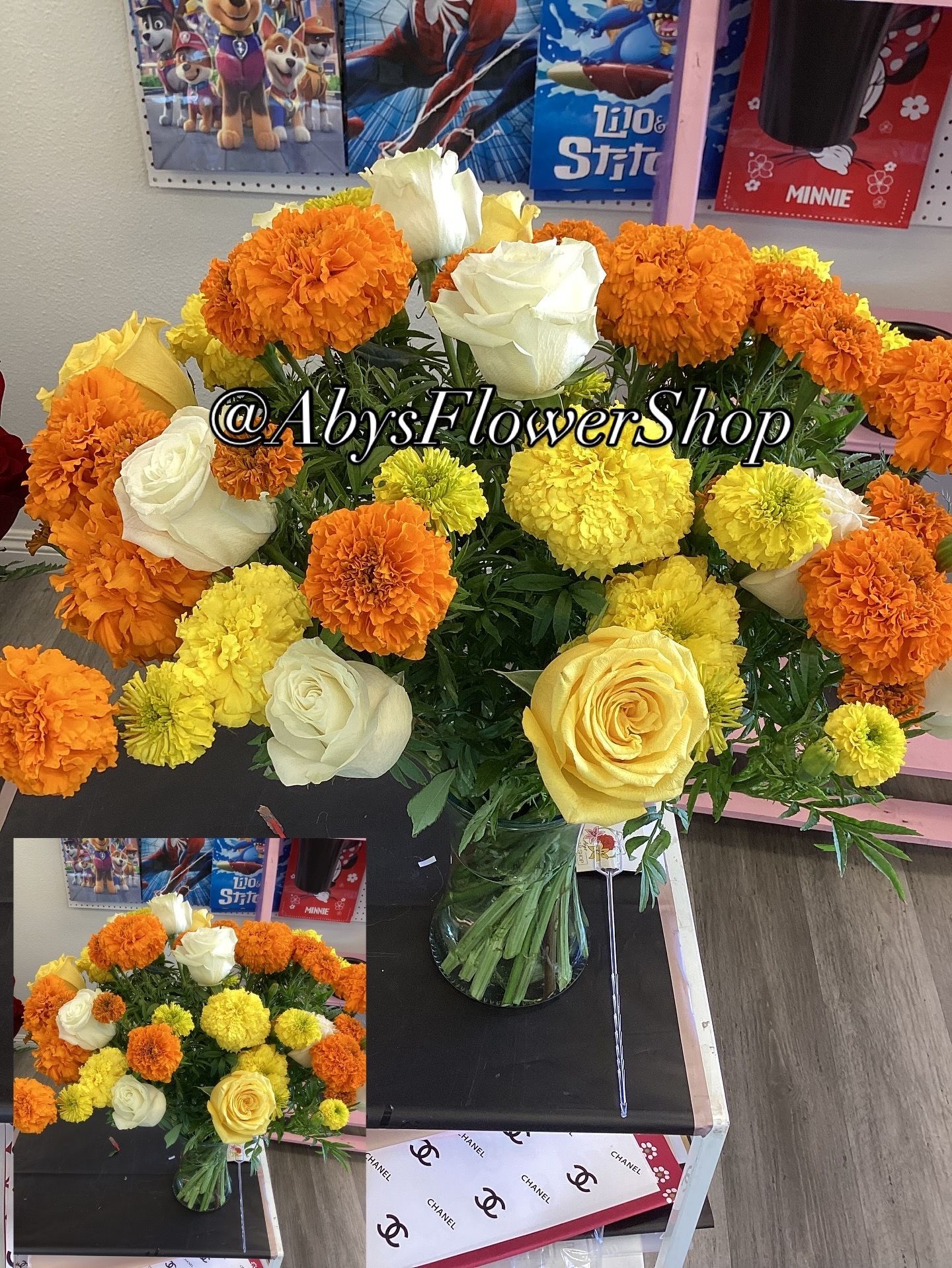 A vibrant bouquet of orange and yellow marigolds mixed with white and yellow roses in a glass vase on a shop counter.