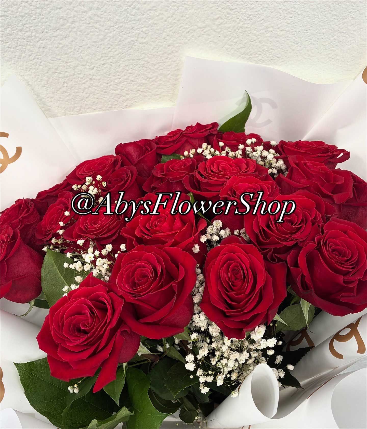 A bouquet of red roses accented with white baby's breath, wrapped in branded white paper.