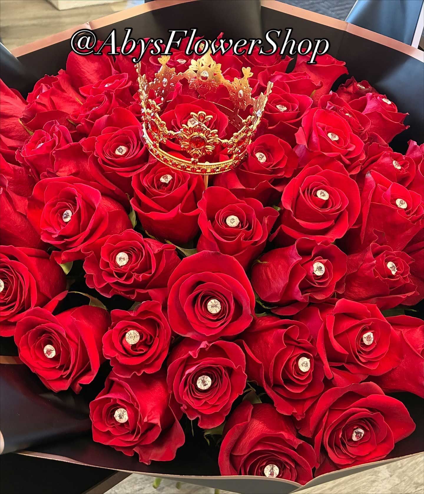 A large bouquet of bright red roses, each with a small diamond-like stud in its center, topped with a decorative crown.