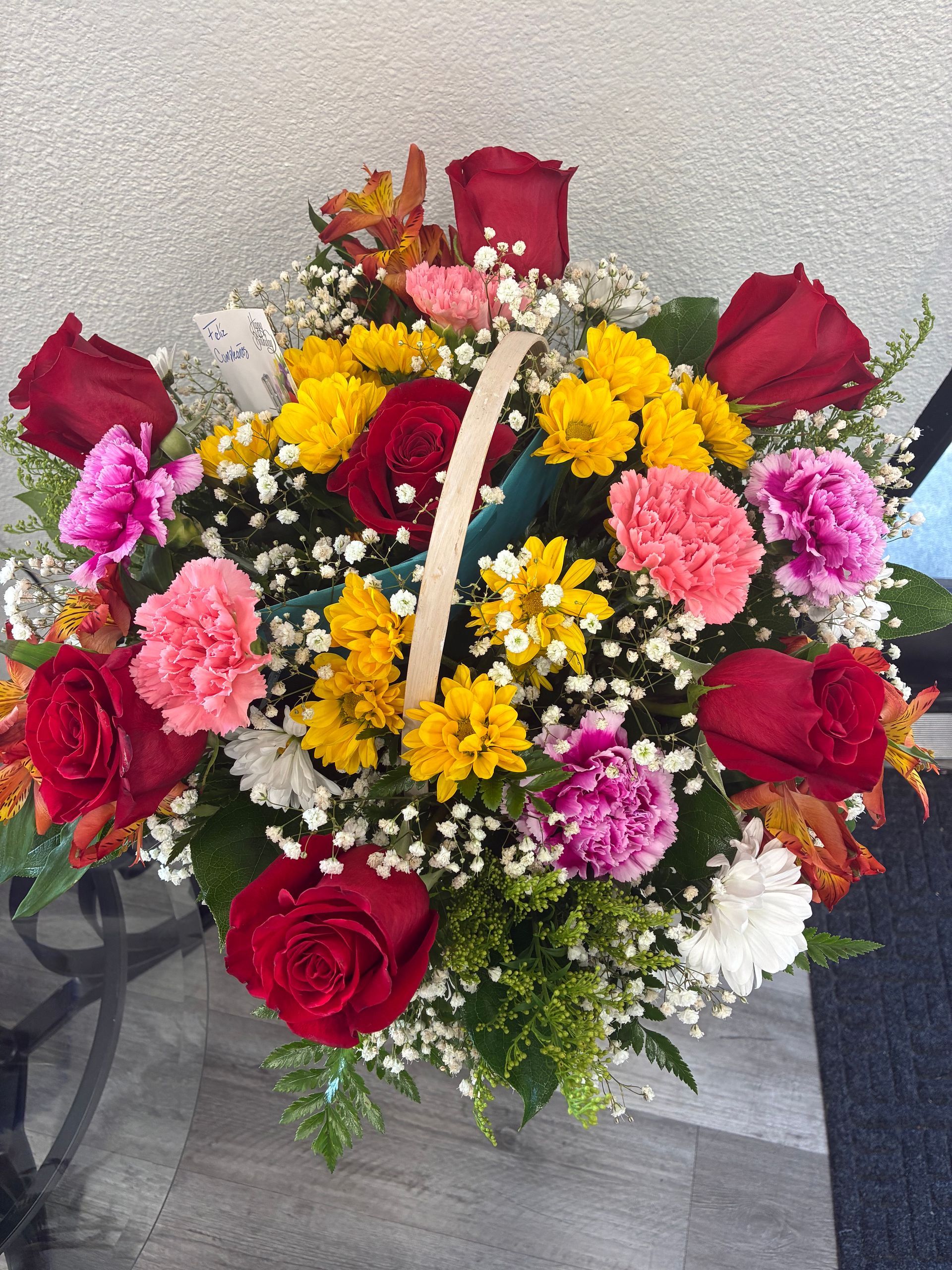 A floral arrangement in a basket with red roses, pink carnations, and yellow chrysanthemums, accented with baby's breath.