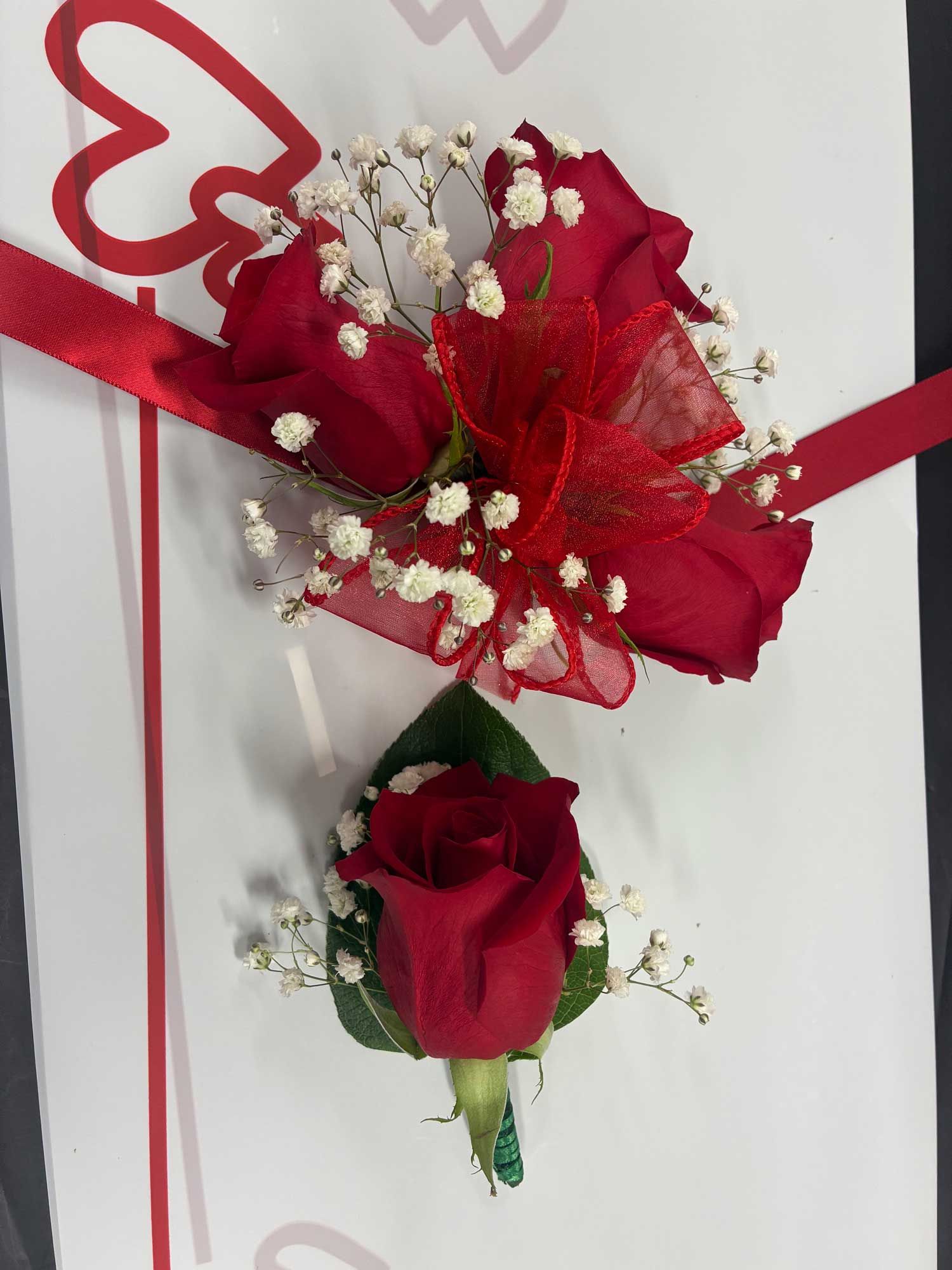 A red rose corsage and matching boutonniere decorated with white baby's breath and a red ribbon on a white background.