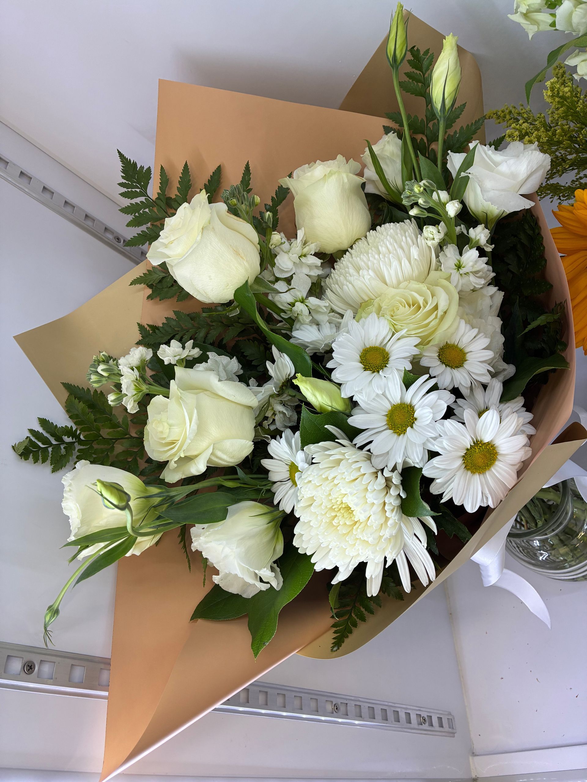 A bouquet of sunflowers, white roses, purple alstroemeria, and daisies, wrapped in green paper with a white ribbon.