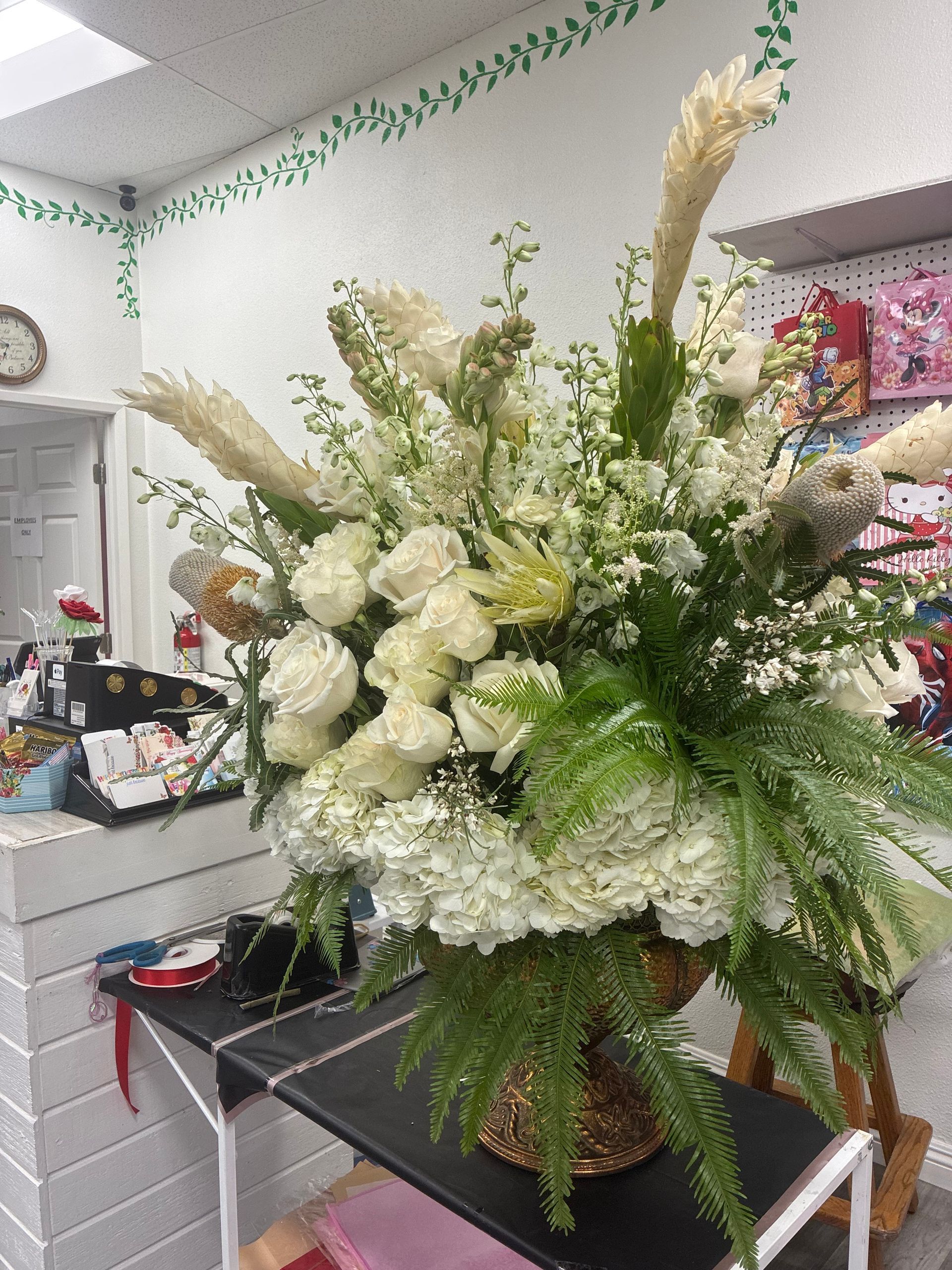 A large, lush floral arrangement of white roses, hydrangeas, and tall feathery stalks in a decorative golden vase.