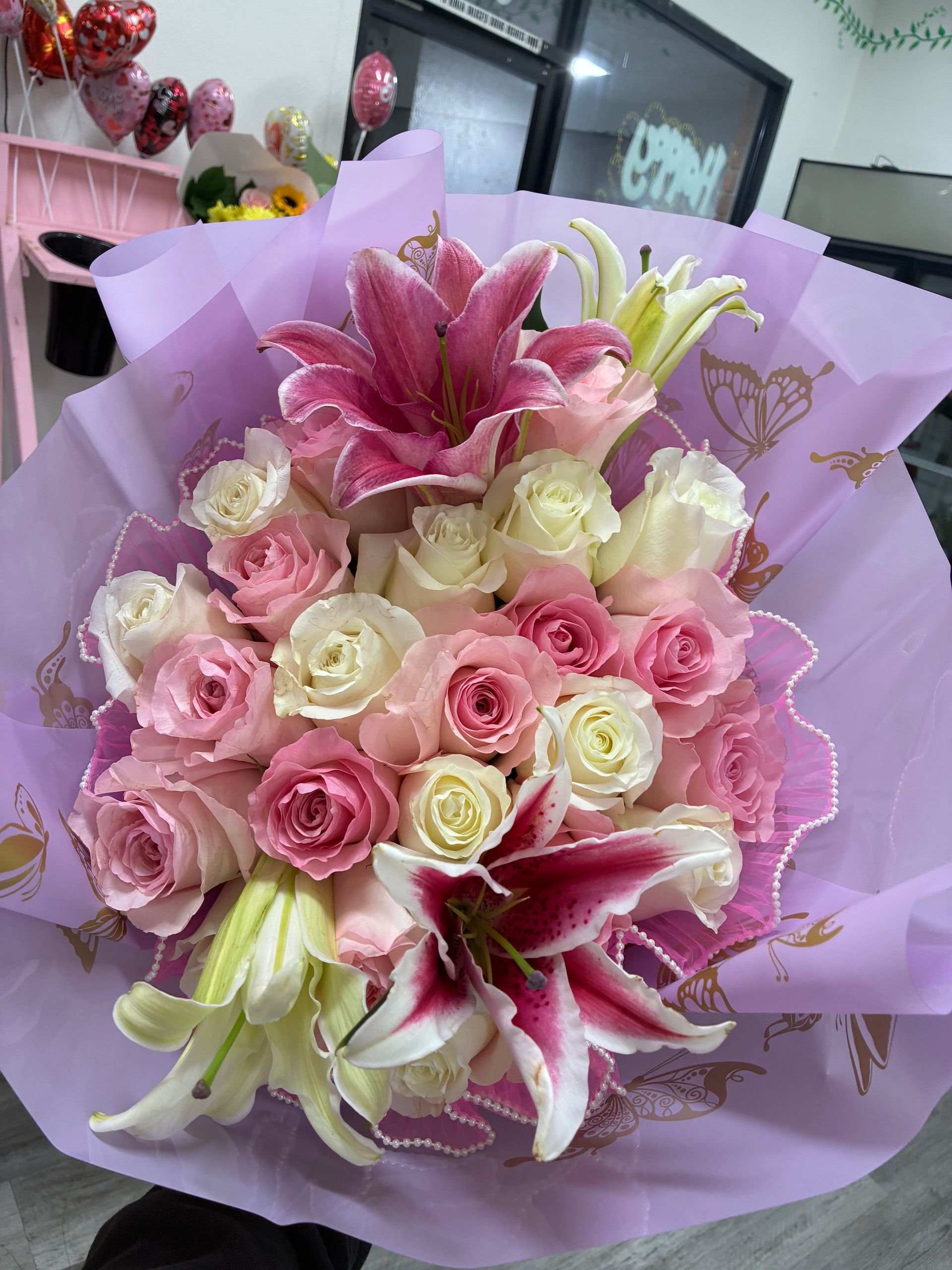 A bouquet of pink and white roses with vibrant pink-and-white stargazer lilies, wrapped in light purple floral paper.