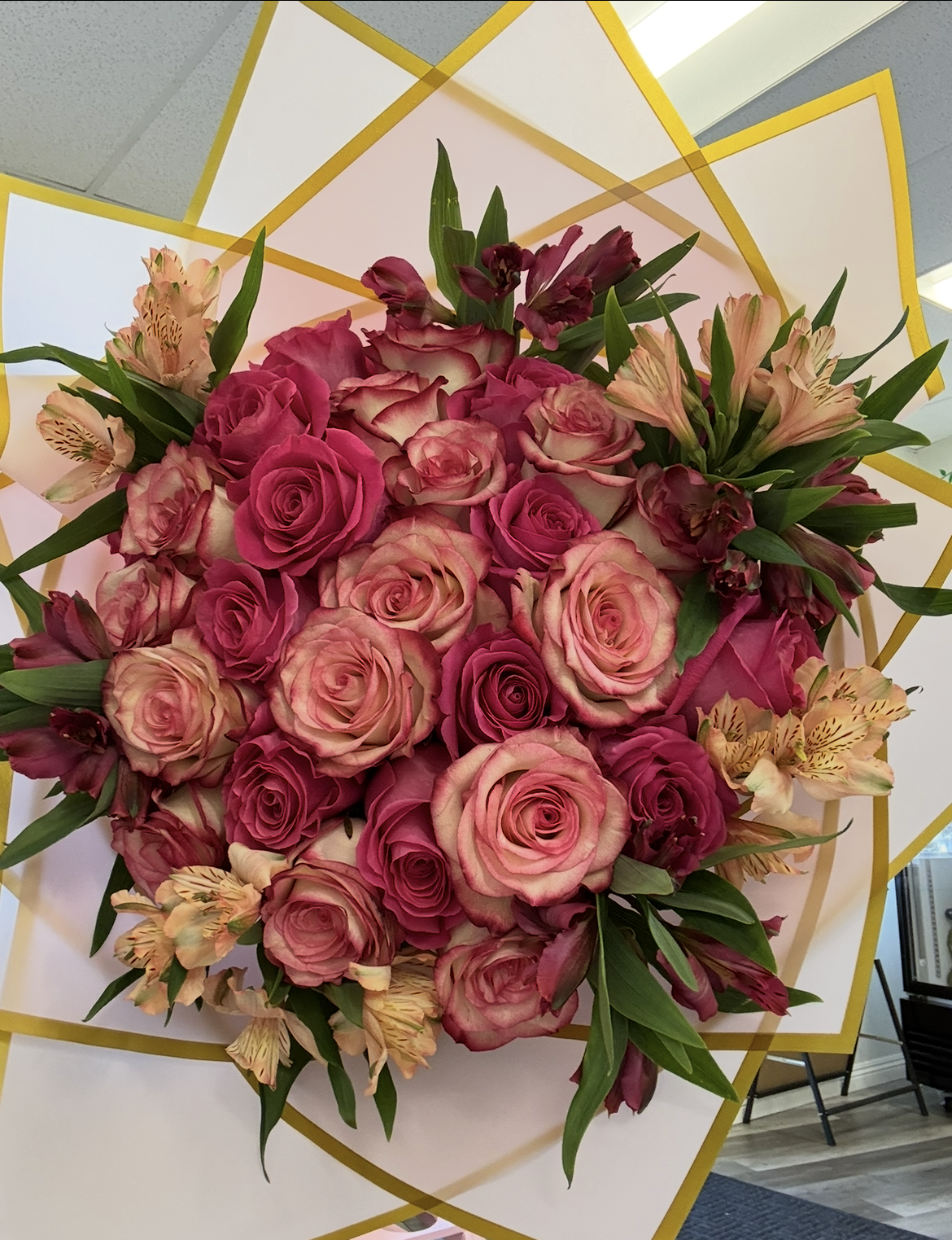 A lush bouquet of pink and peach roses accented with alstroemeria, wrapped in white and gold geometric paper.