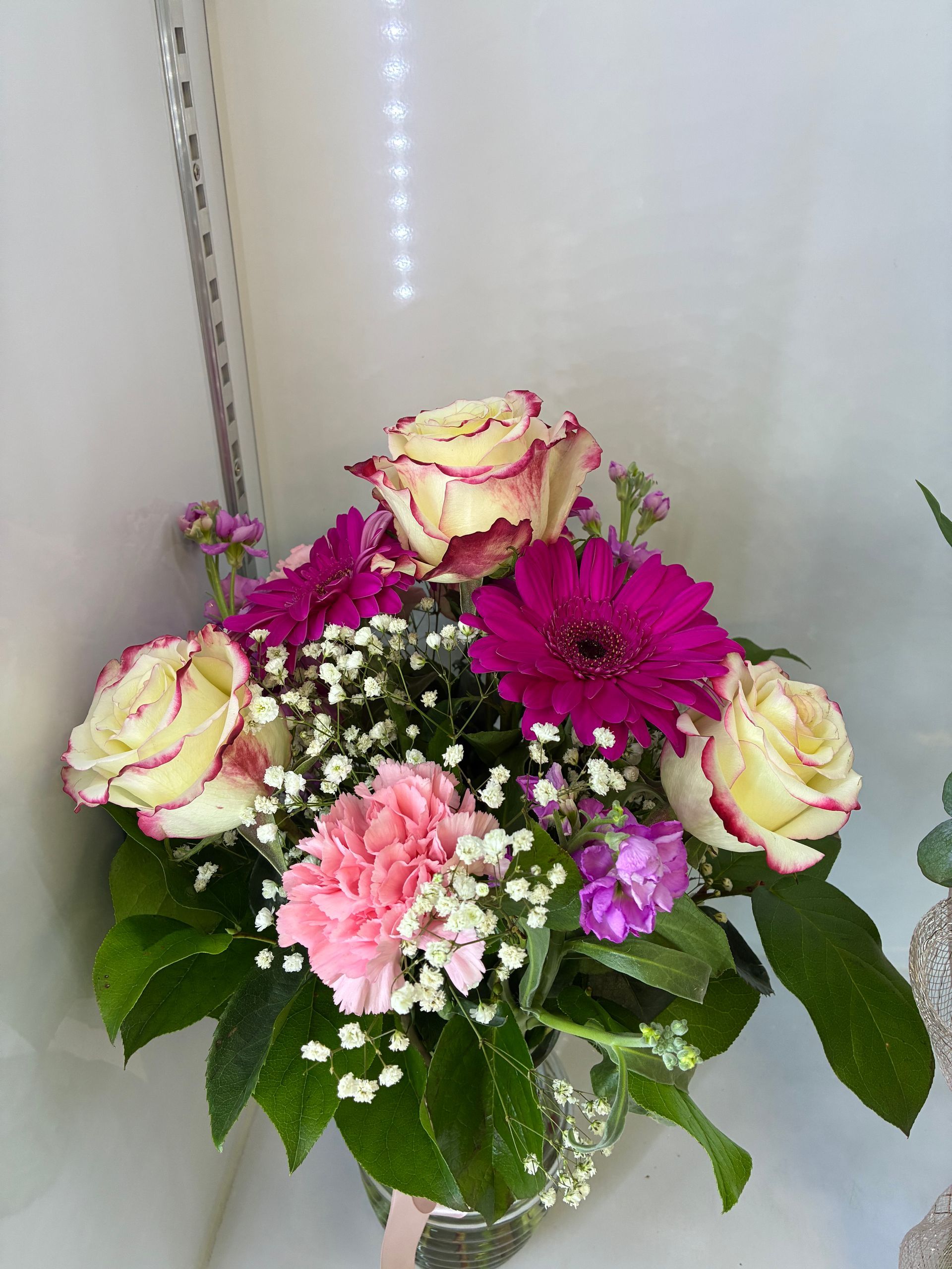 A bouquet of cream roses with pink edges, deep pink gerbera daisies, a pink carnation, and baby's breath in a glass vase.