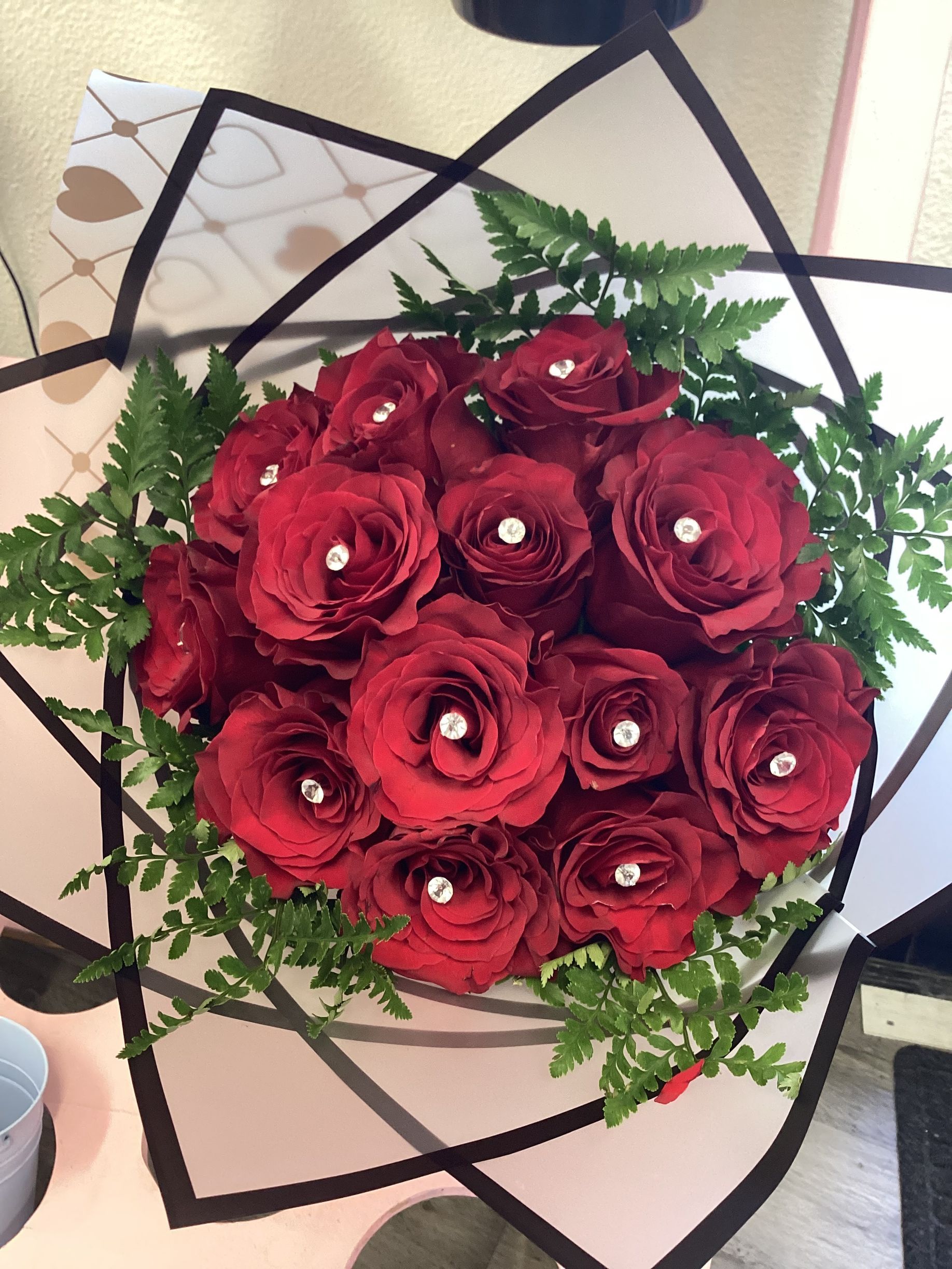 A bouquet of deep red roses with small crystal accents, wrapped in white paper with a bold black geometric trim.