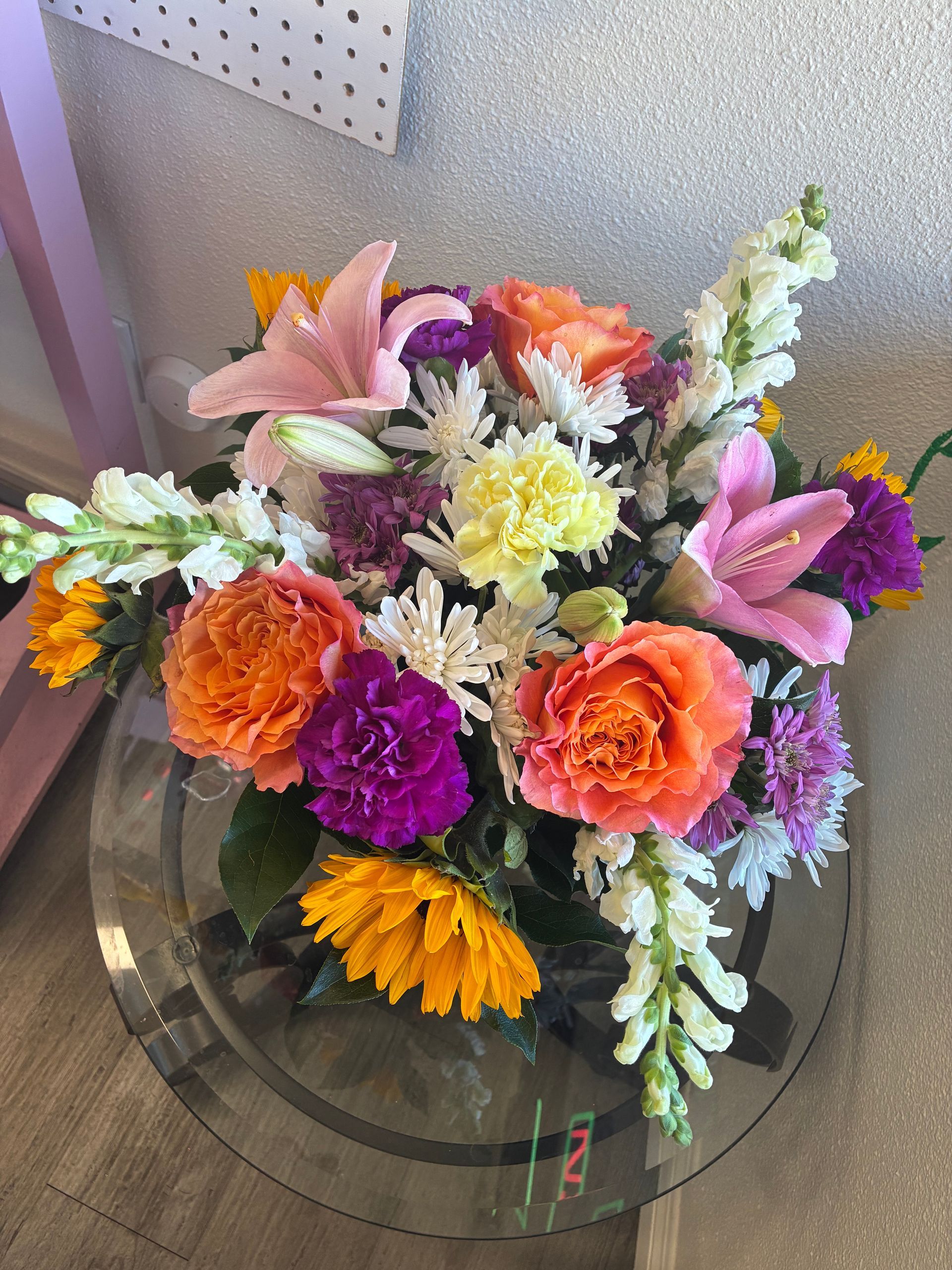 A colorful floral arrangement in shades of orange, yellow, pink, and purple, sitting on a glass-topped table.