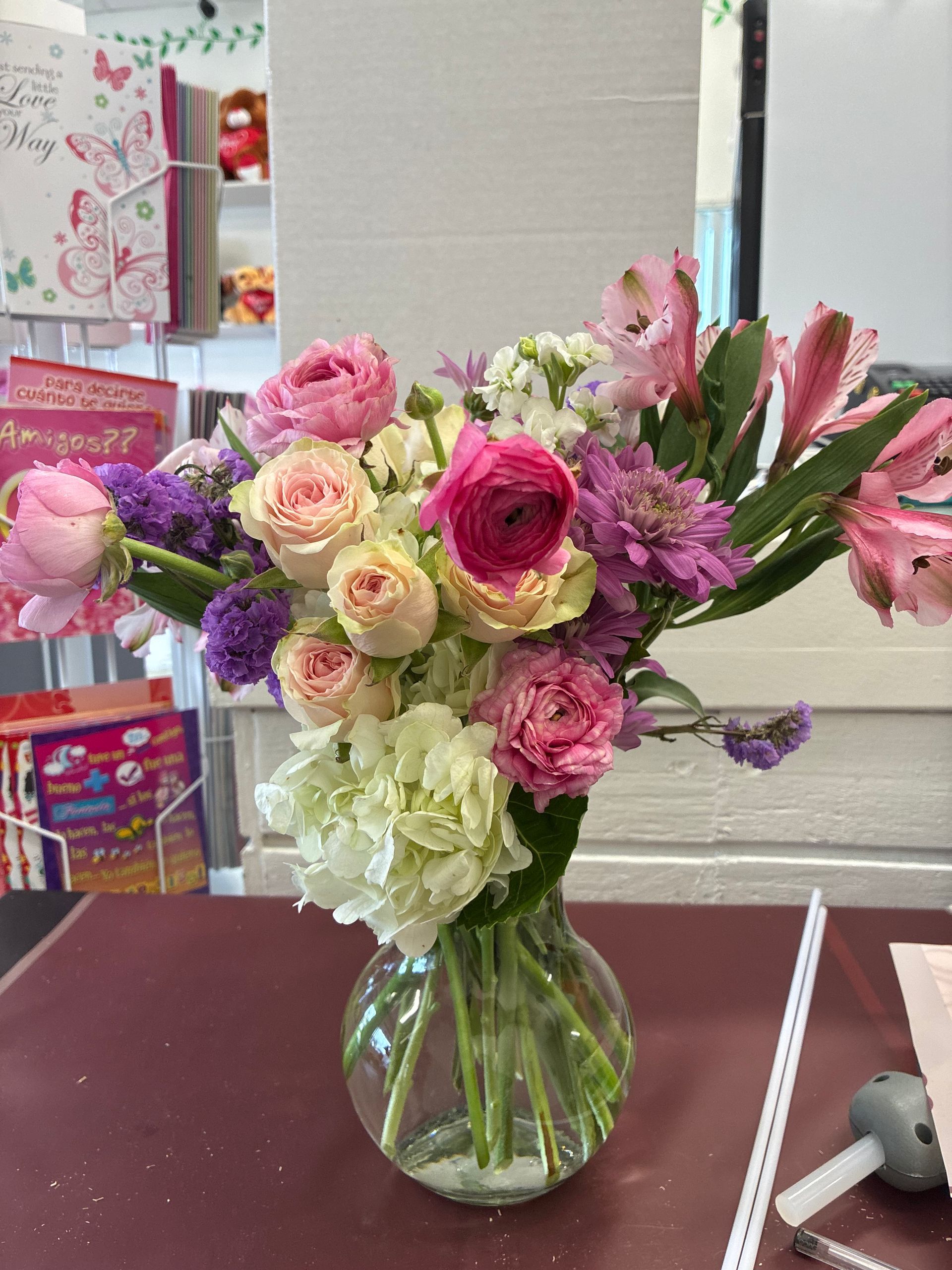 A clear glass vase filled with a vibrant bouquet of pink, white, and purple flowers sits on a table.