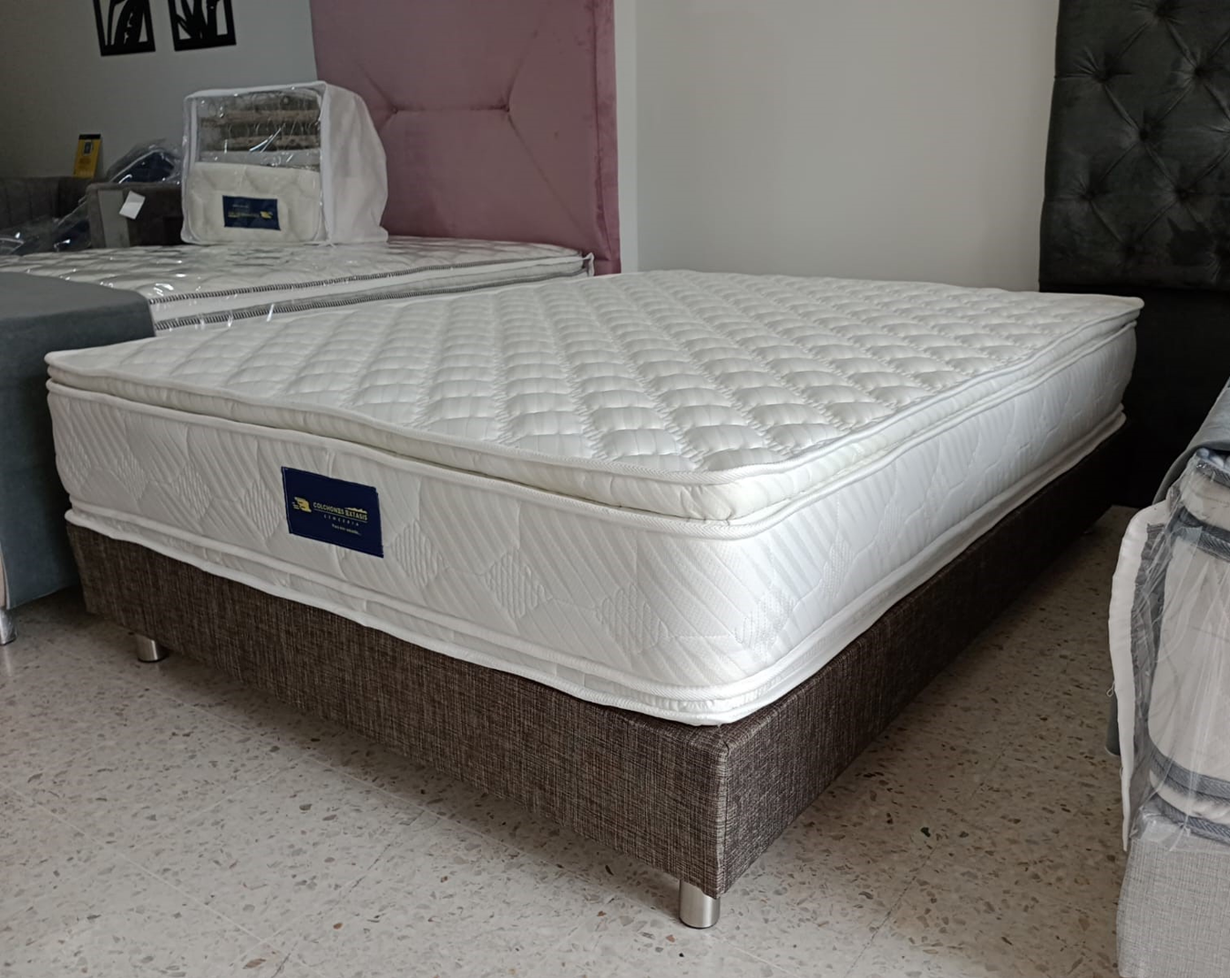 Colchón blanco acolchado sobre una base de cama marrón, en un dormitorio con cabeceros capitoné