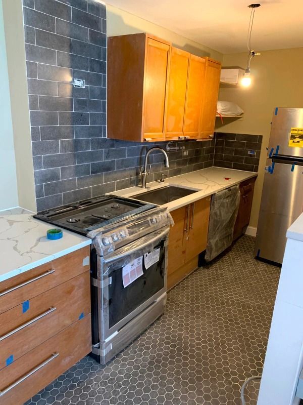 Kitchen with newly installed dark tiled backsplash, light countertops, and wooden cabinets.