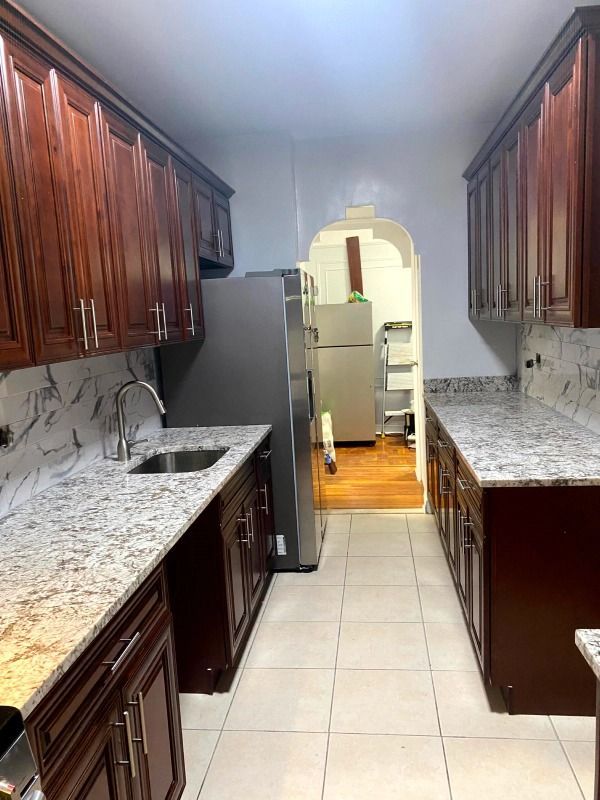 Narrow kitchen with dark wood cabinets, granite countertops, and stainless steel refrigerator.