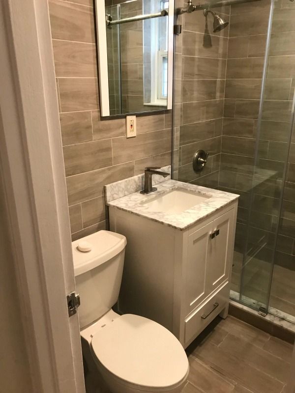 Bathroom with white vanity, toilet, and shower. Tile walls and floor, glass shower door.