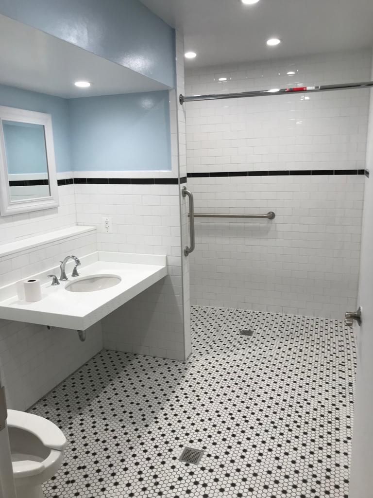 Accessible bathroom with a glass shower, white tiles, and black and white patterned floor.
