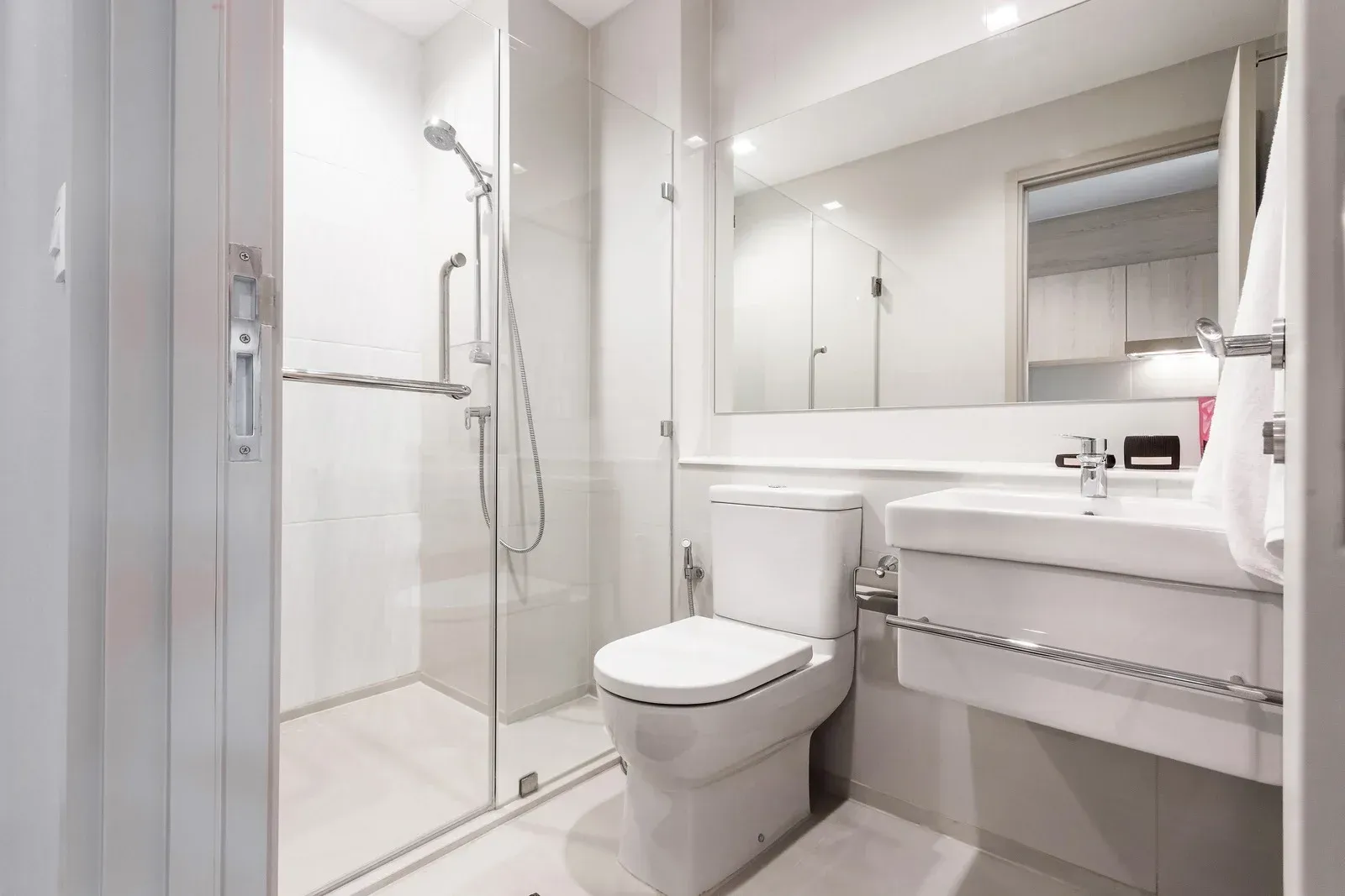 Modern white bathroom with a shower, toilet, sink, and large mirror.