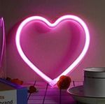 Pink neon heart light on a wall; a cup and rose accents on a table.