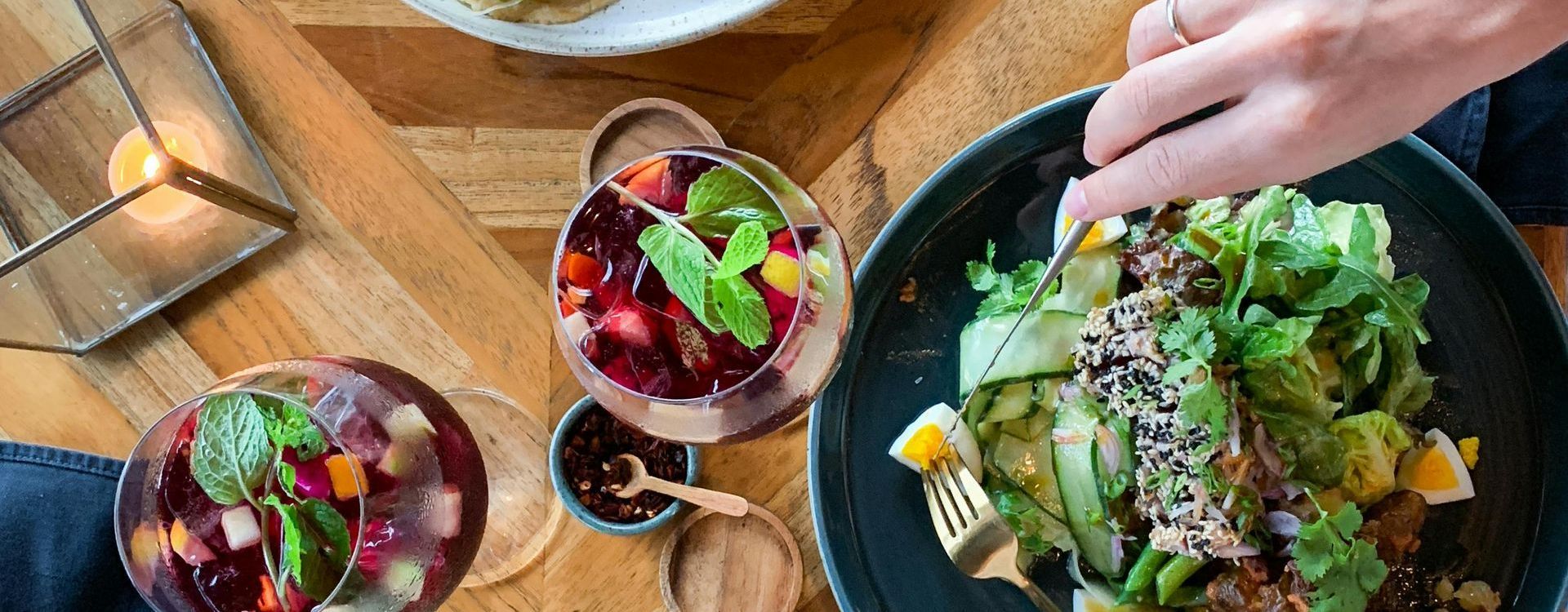 Overhead shot of a table with food and drink. A person is eating a salad with a fork.