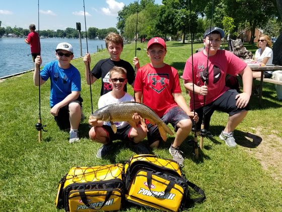 A group of young boys are holding fishing rods and a large fish.