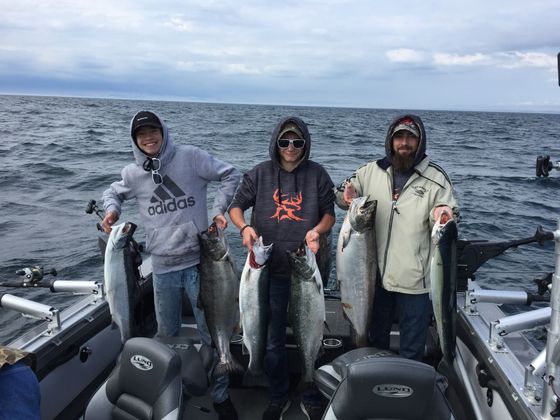 Three men are standing on a boat holding fish.