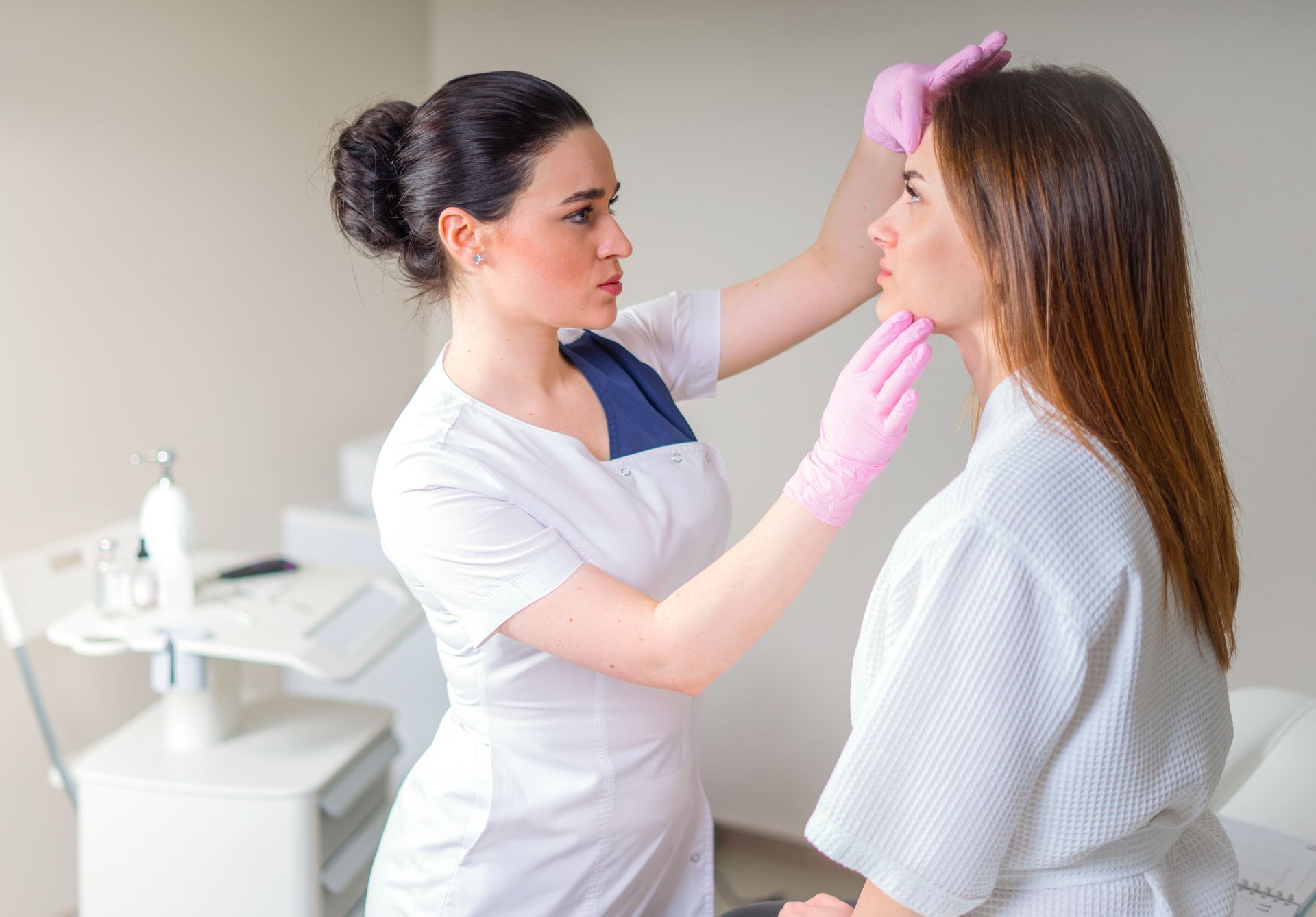 Doctor examining a patient's face in a bright clinic, wearing pink gloves